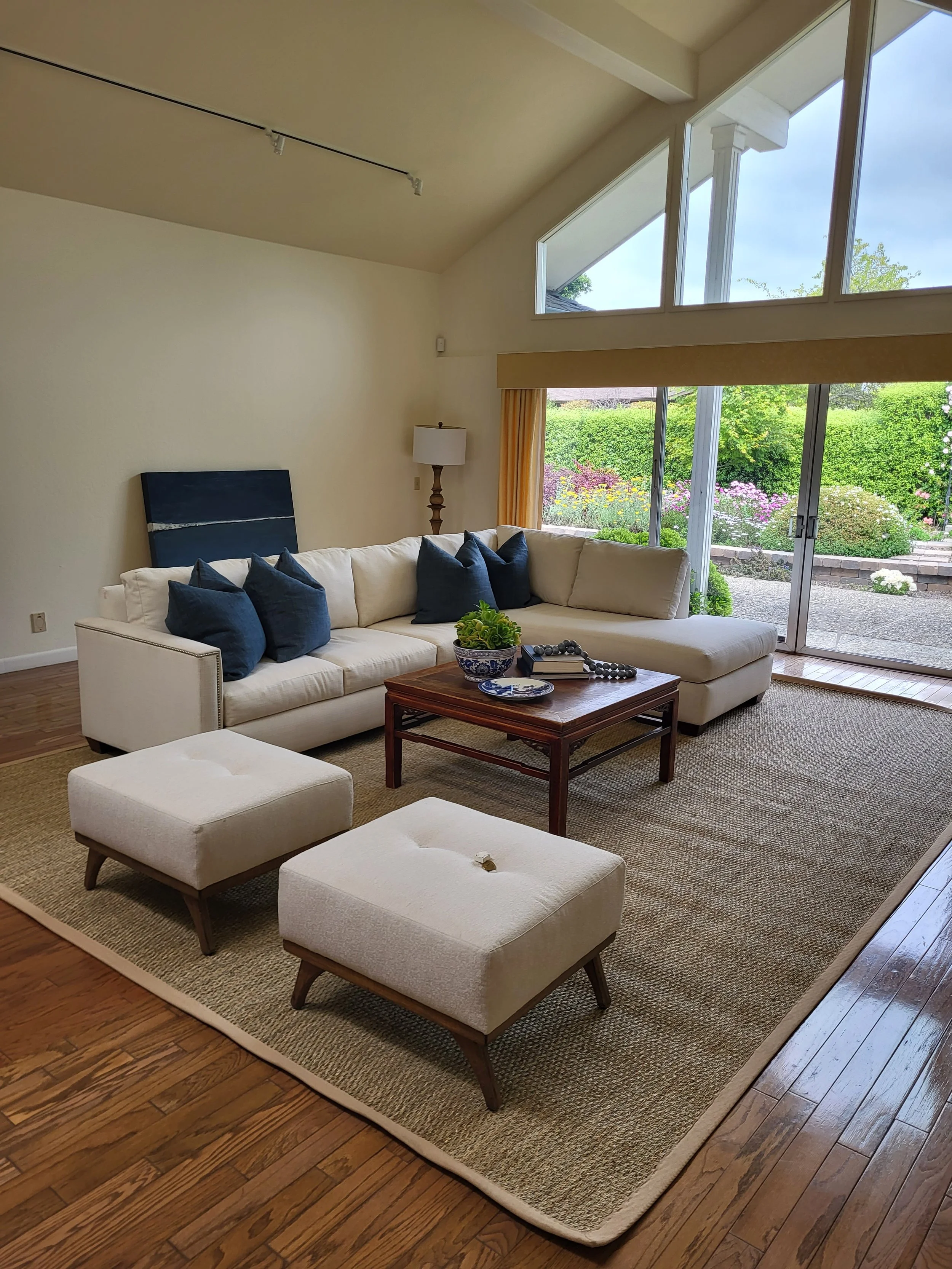 Image shows the inside of a living room with open sliding doors, and a sand colored L-shaped couch