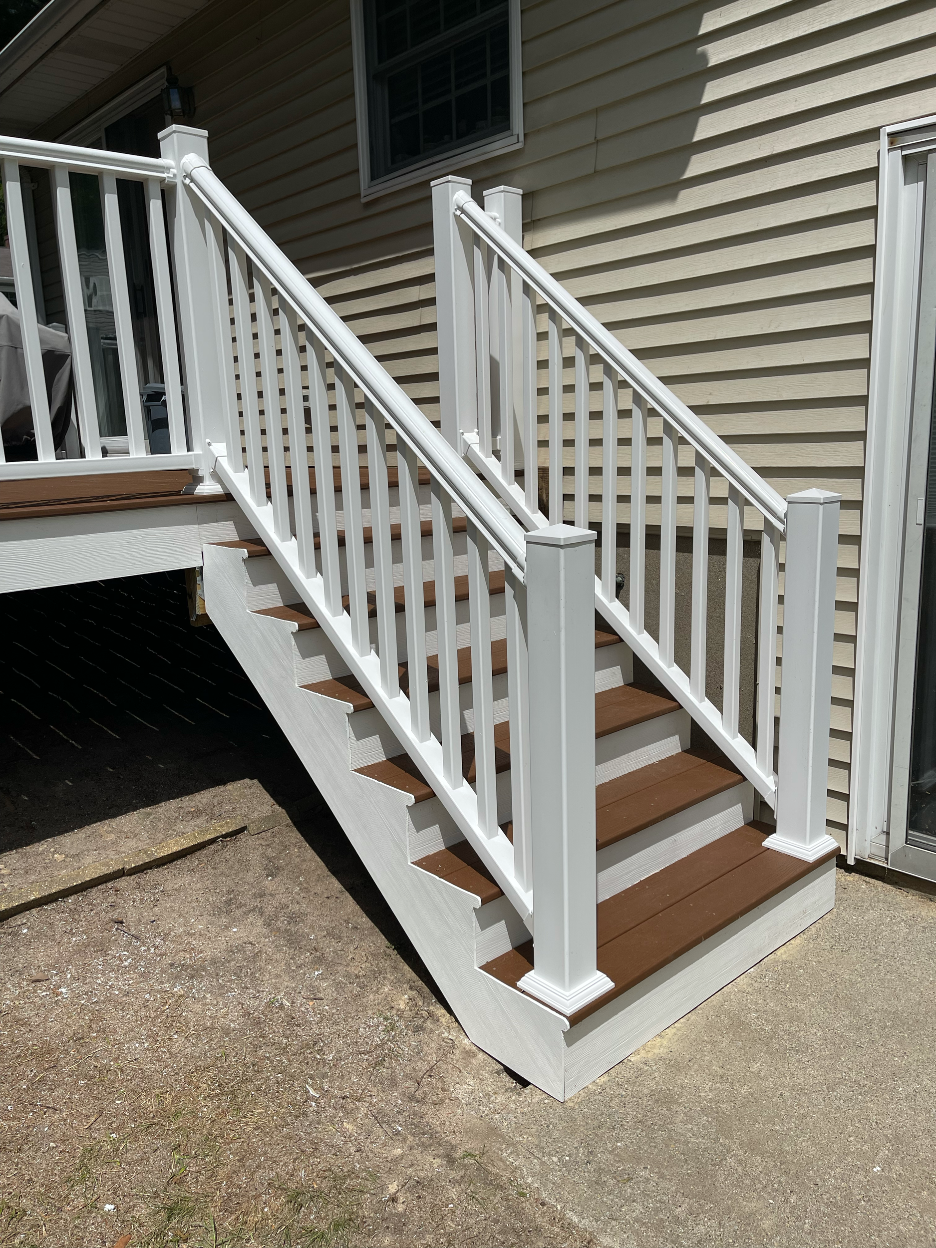 Exterior view of a newly built wooden deck with white railings and stairs attached to a house with beige siding.