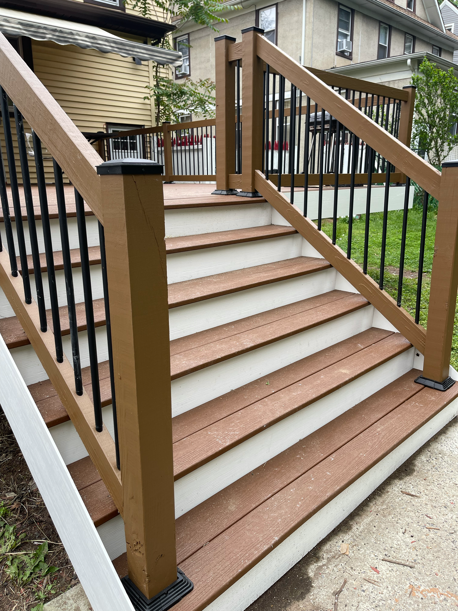 Wooden stairs with black metal railings leading up to a deck in a backyard.