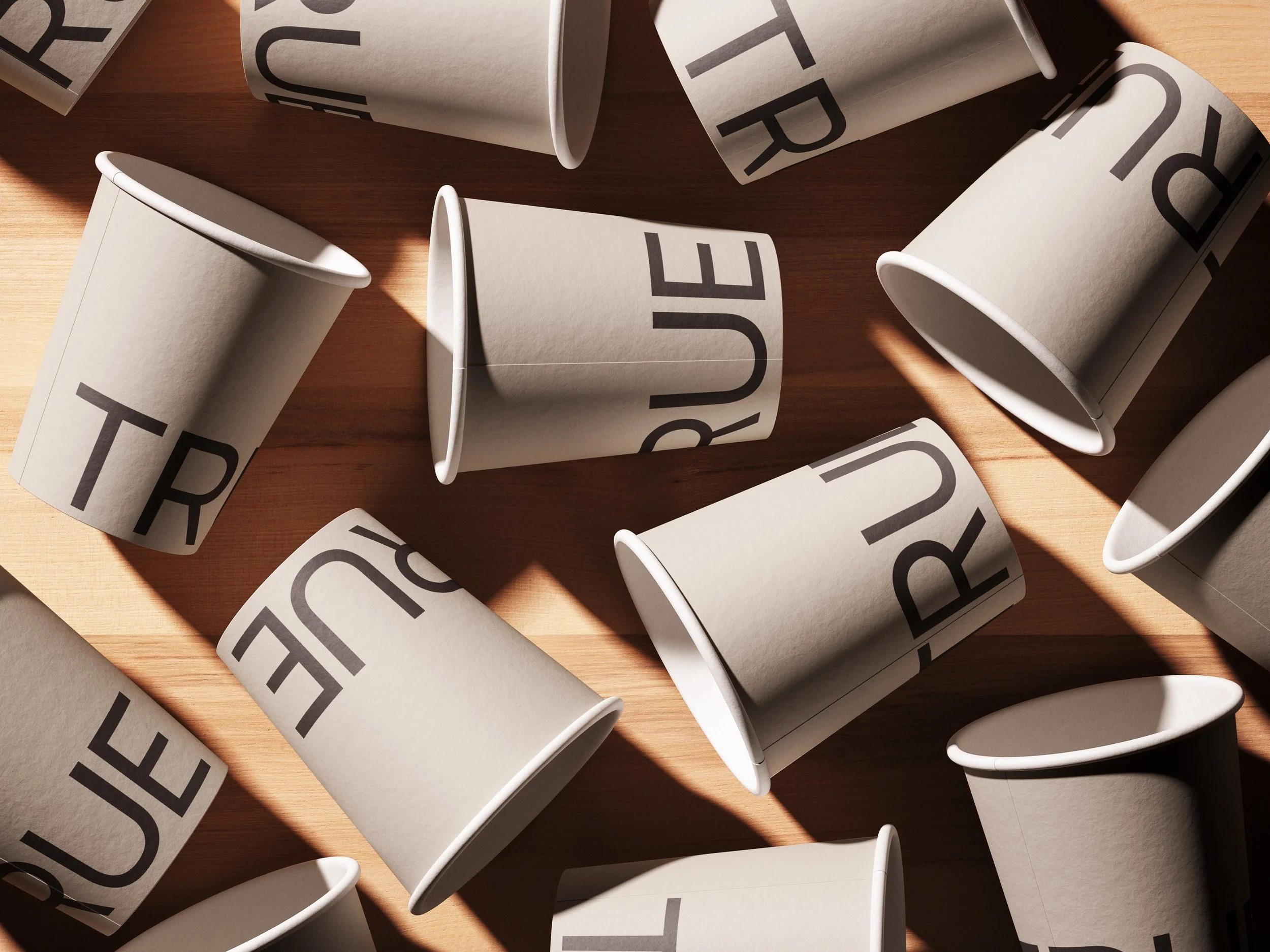 TRUE Comms branded paper cups scattered on a wooden surface, featuring the TRUE secondary wordmark in espresso — an experiential brand touchpoint concept for conference and event sponsorships.