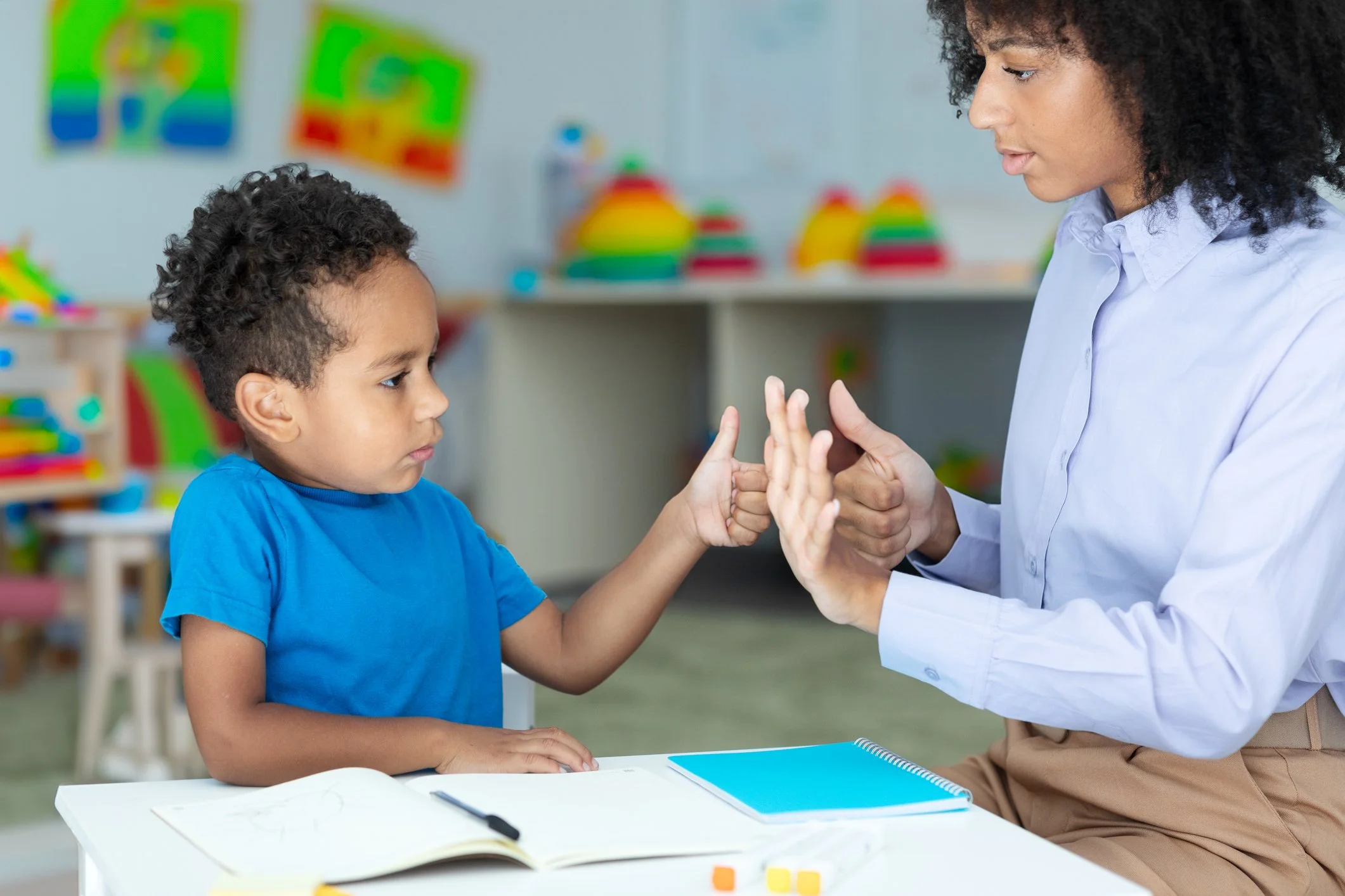 A young boy and a woman are giving each other a high five in a classroom.