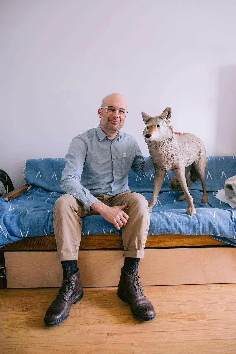 A person sits on a blue couch with hand on a realistic plastic coyote.
