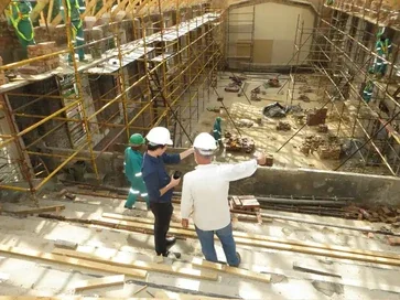 Construction workers in safety gear on a building site with scaffolding and construction materials.