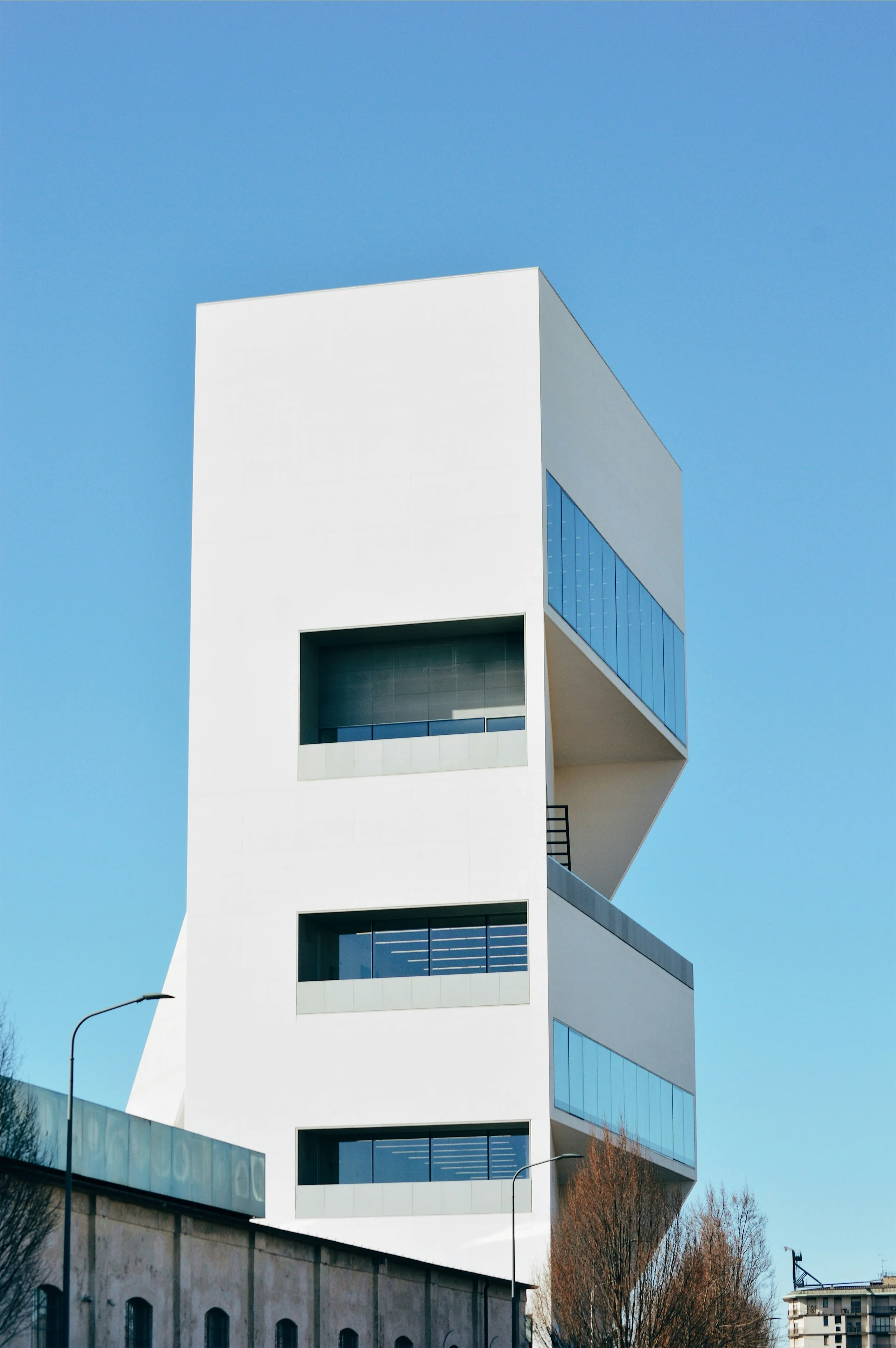 Modern white building with large glass windows and geometric design, with a clear blue sky background.