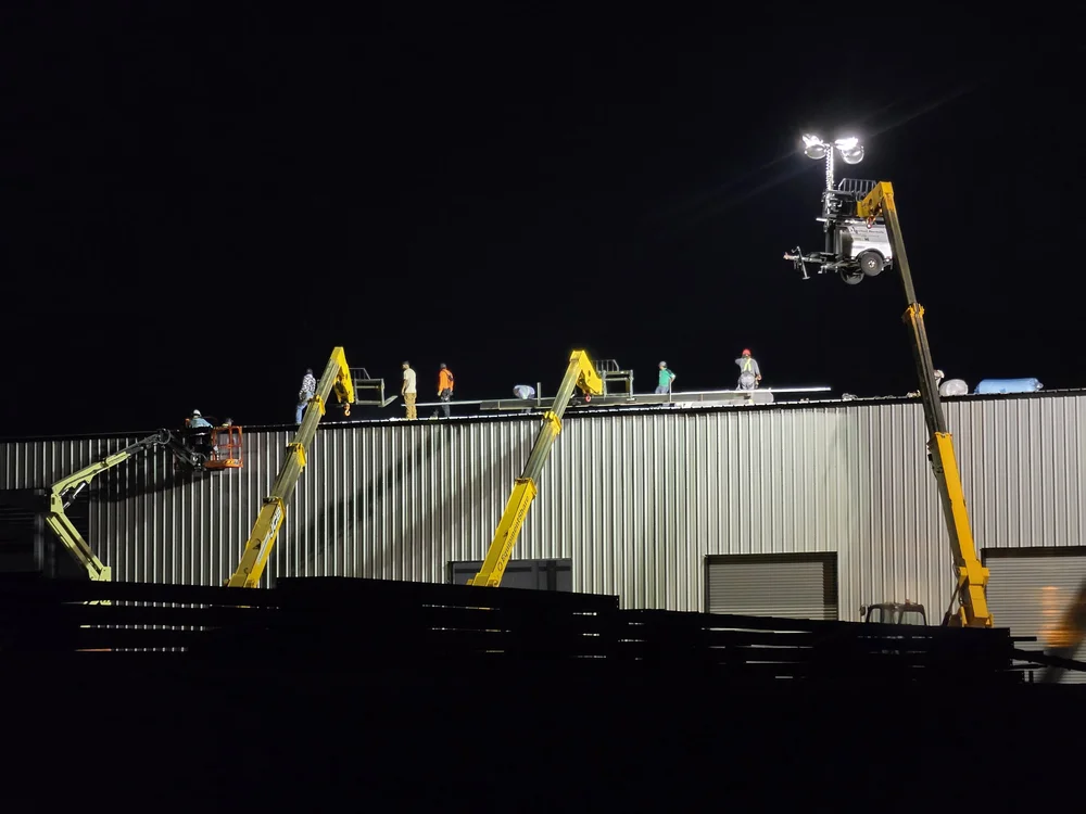 Night shift roof crew under light towers on a data center staging building