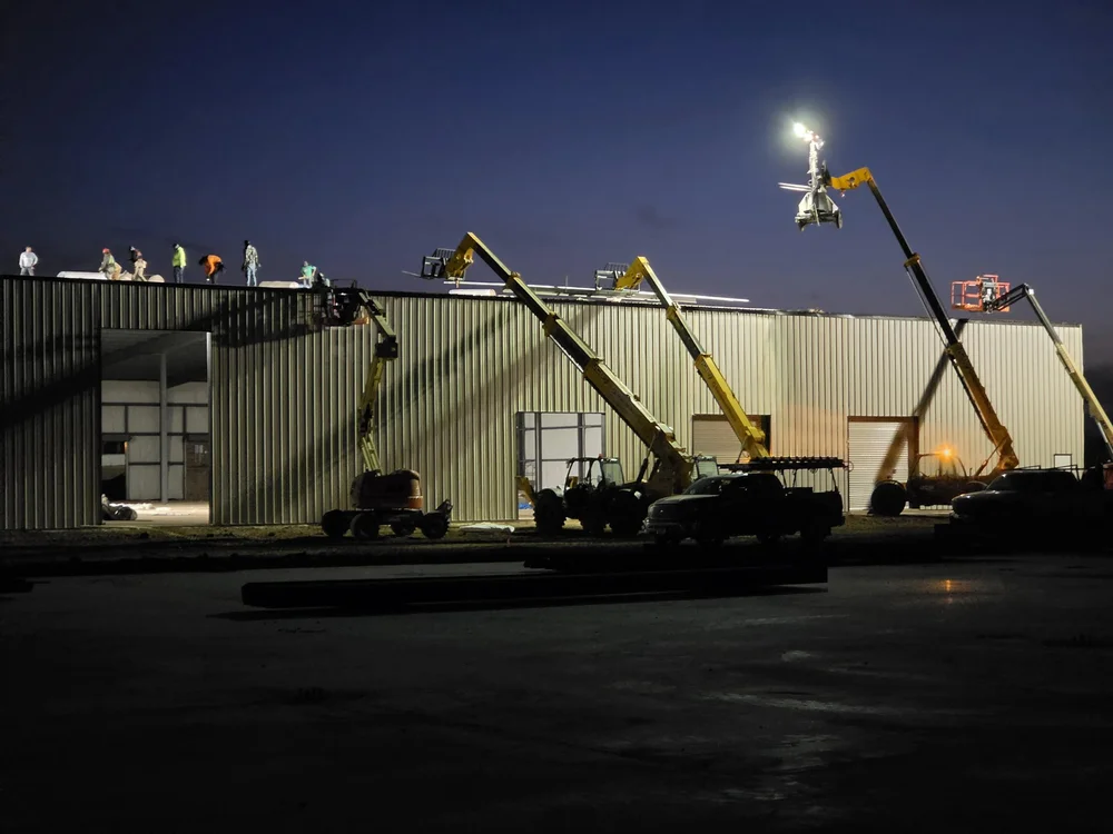 Roof and wall crews working before sunrise on a data center support building