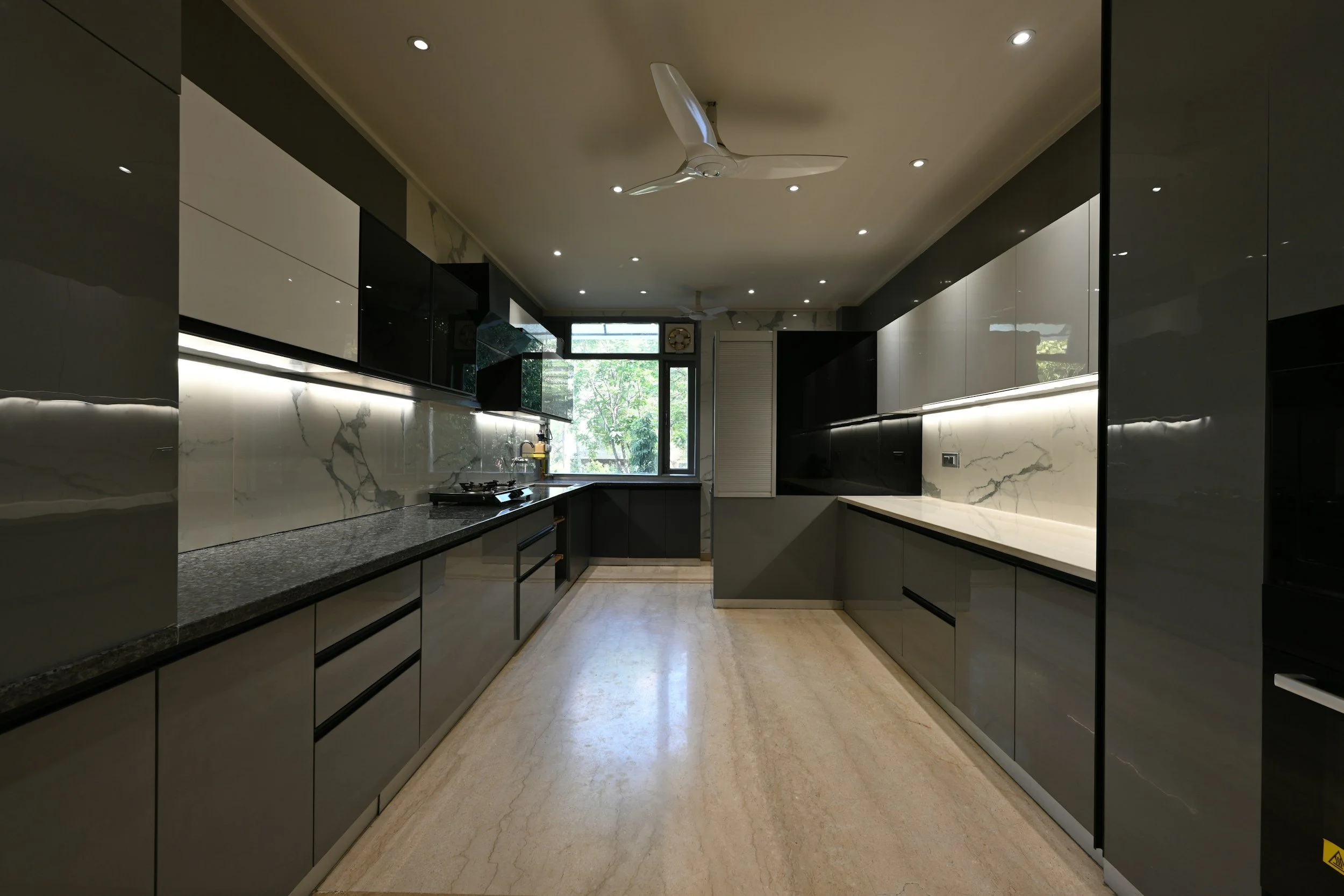 Modern kitchen with dark and light cabinetry, marble backsplash, granite countertops, and a large window showing trees outside.