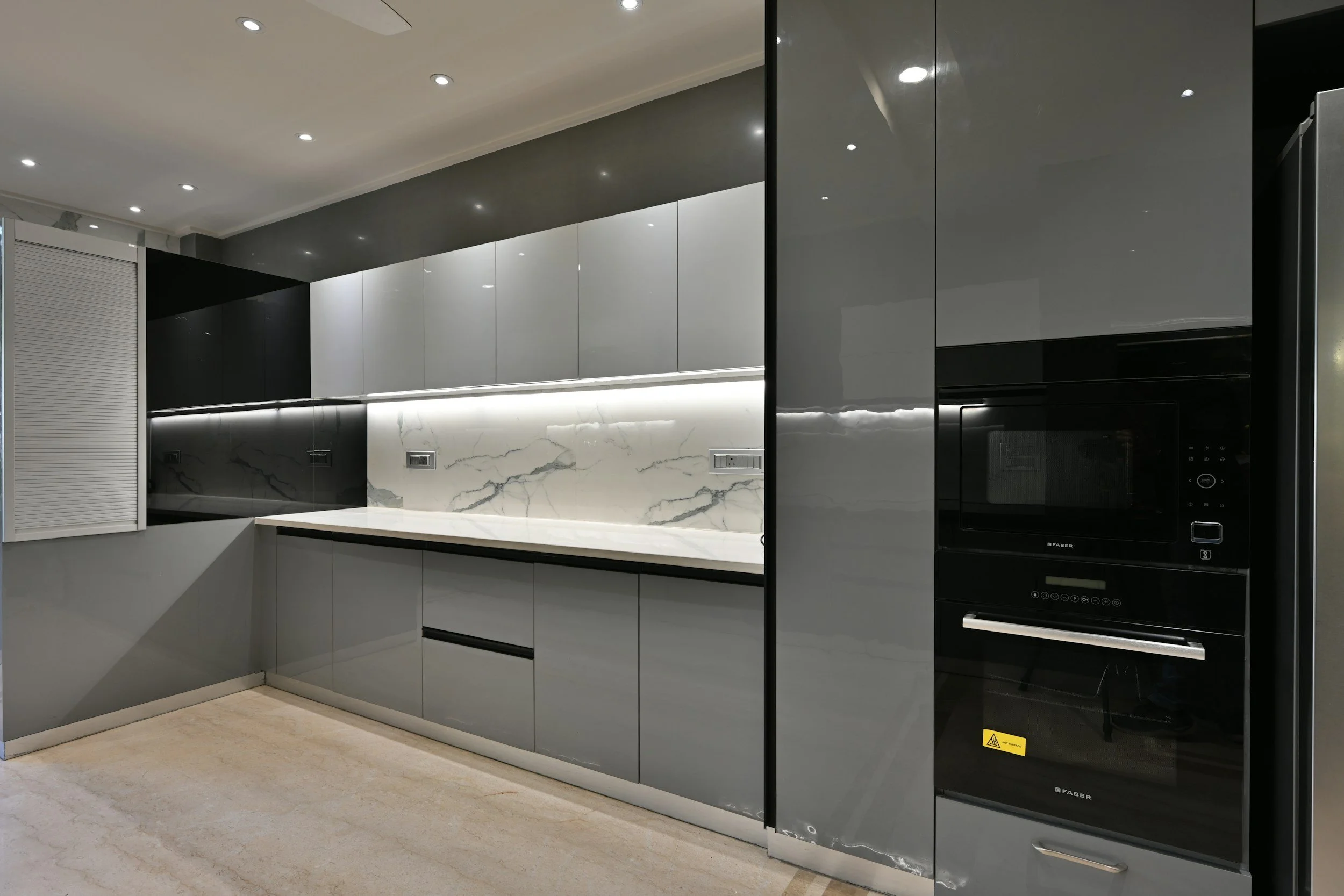 Modern kitchen with grey cabinets, marble backsplash, and built-in black microwave oven.