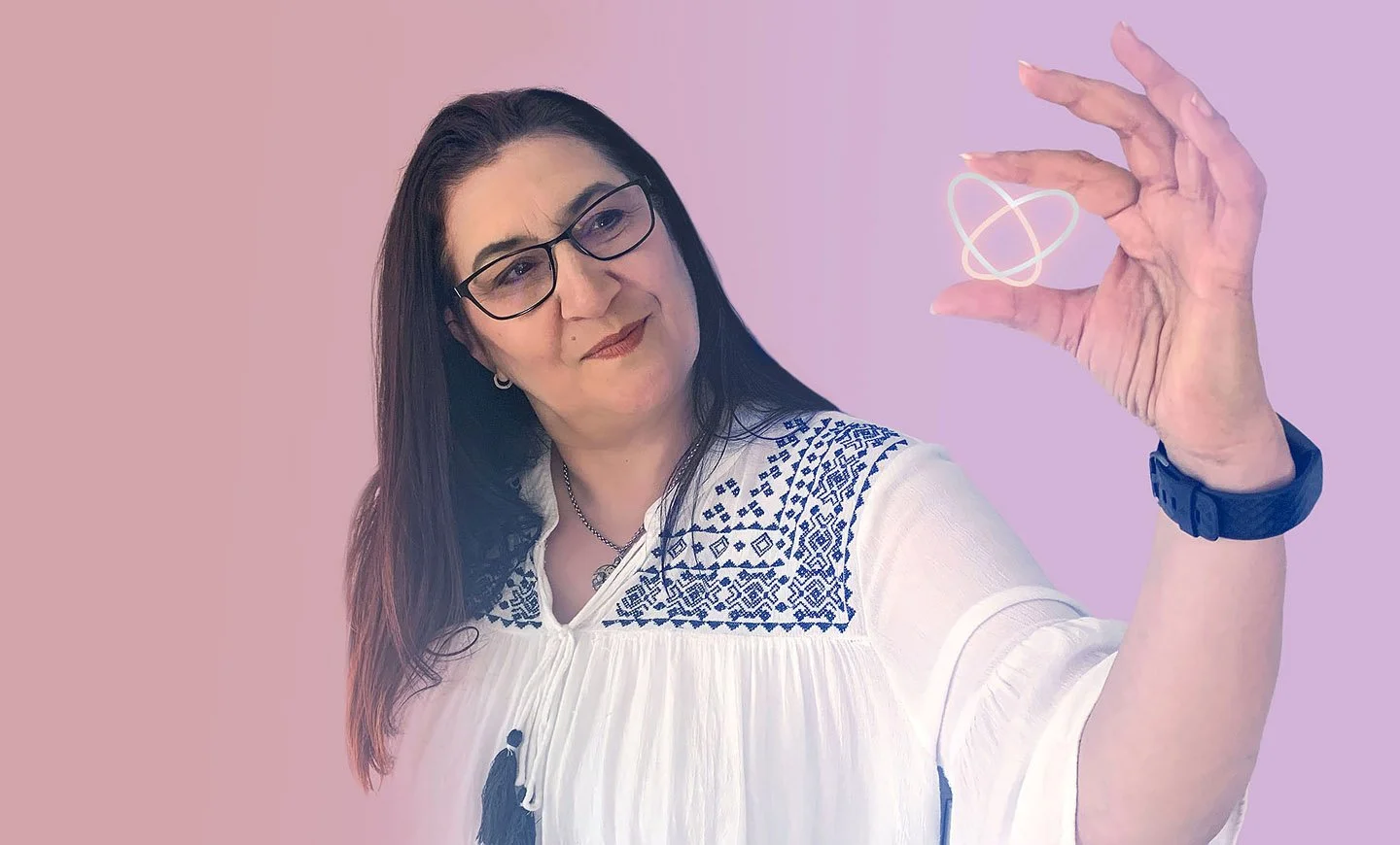 A woman with glasses and dark hair holding a glowing digital atom model in her hand, standing against a pastel pink and purple background.