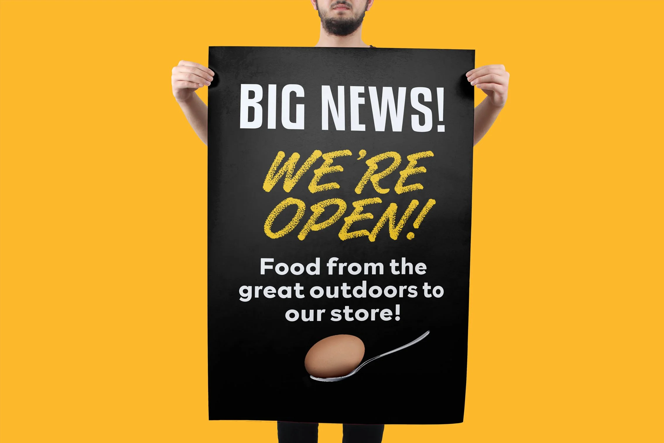 A man holding up a protest board, on a yellow background. The board features is a message to customers that a new store is open for business.