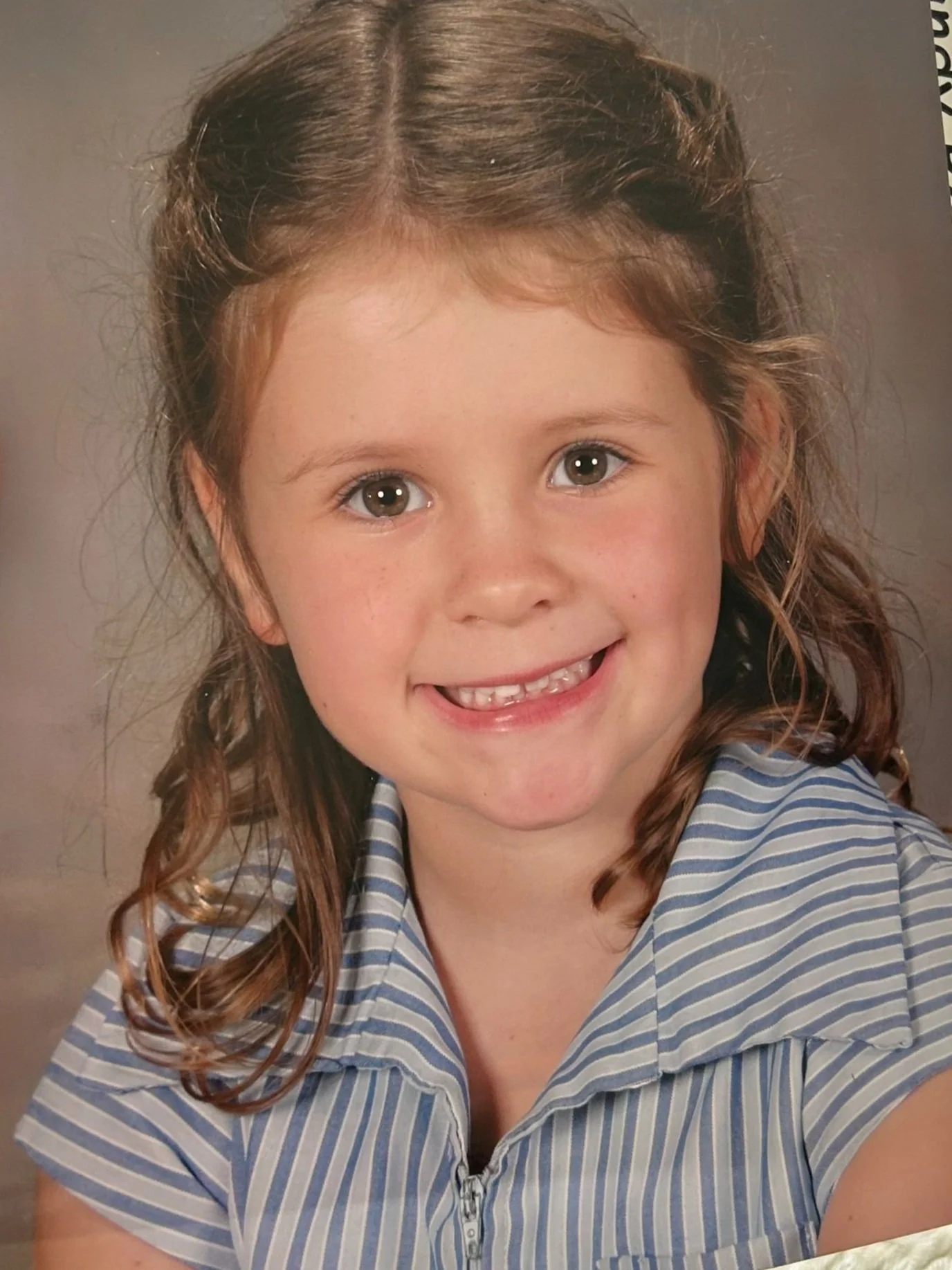 Young girl smiling in striped shirt, school portrait.