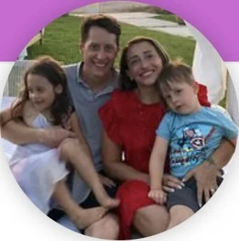 Family portrait with parents and two children sitting outdoors on a grassy area.