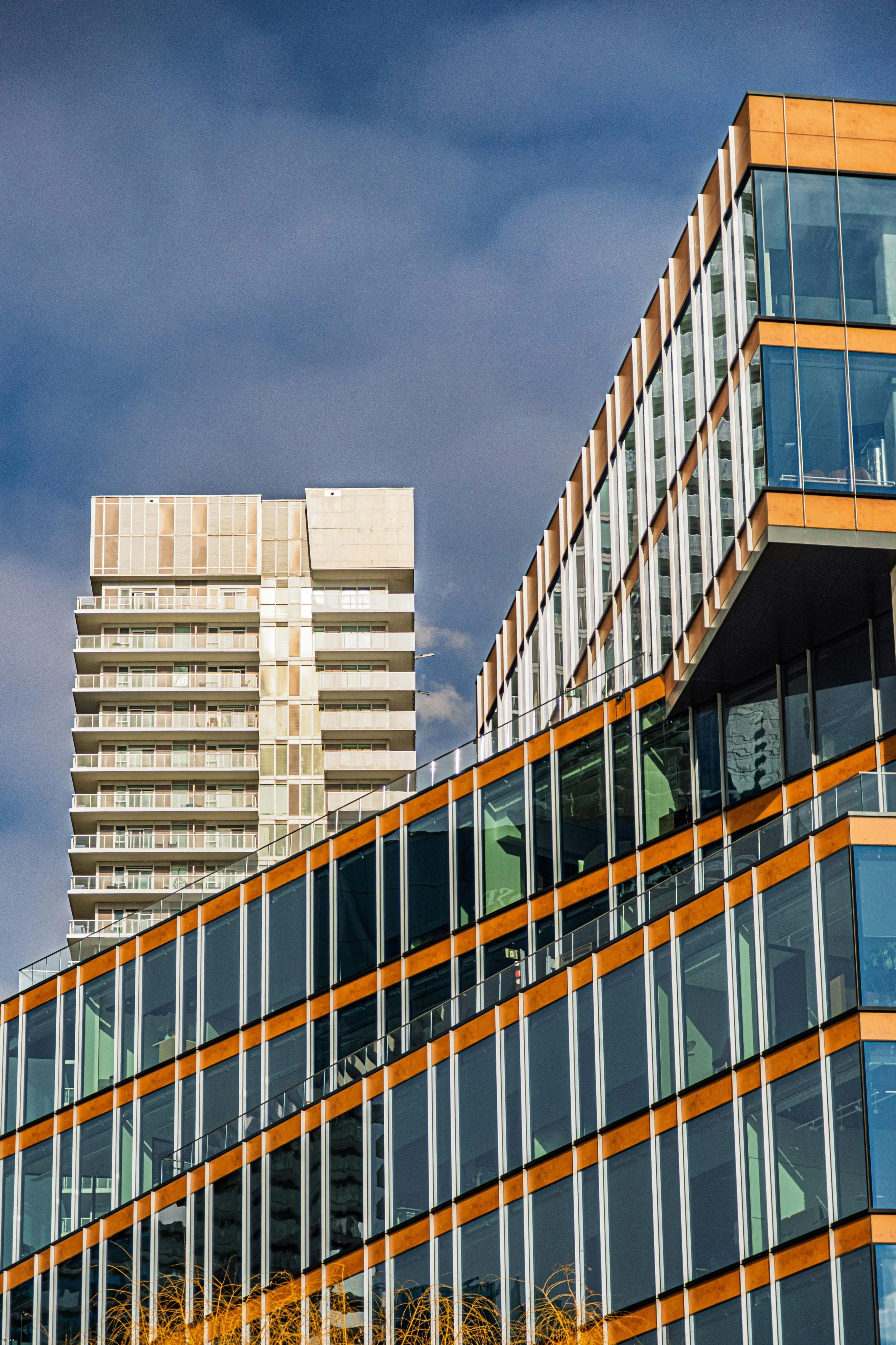 Modern high-rise buildings with glass windows and orange accents against a cloudy sky.