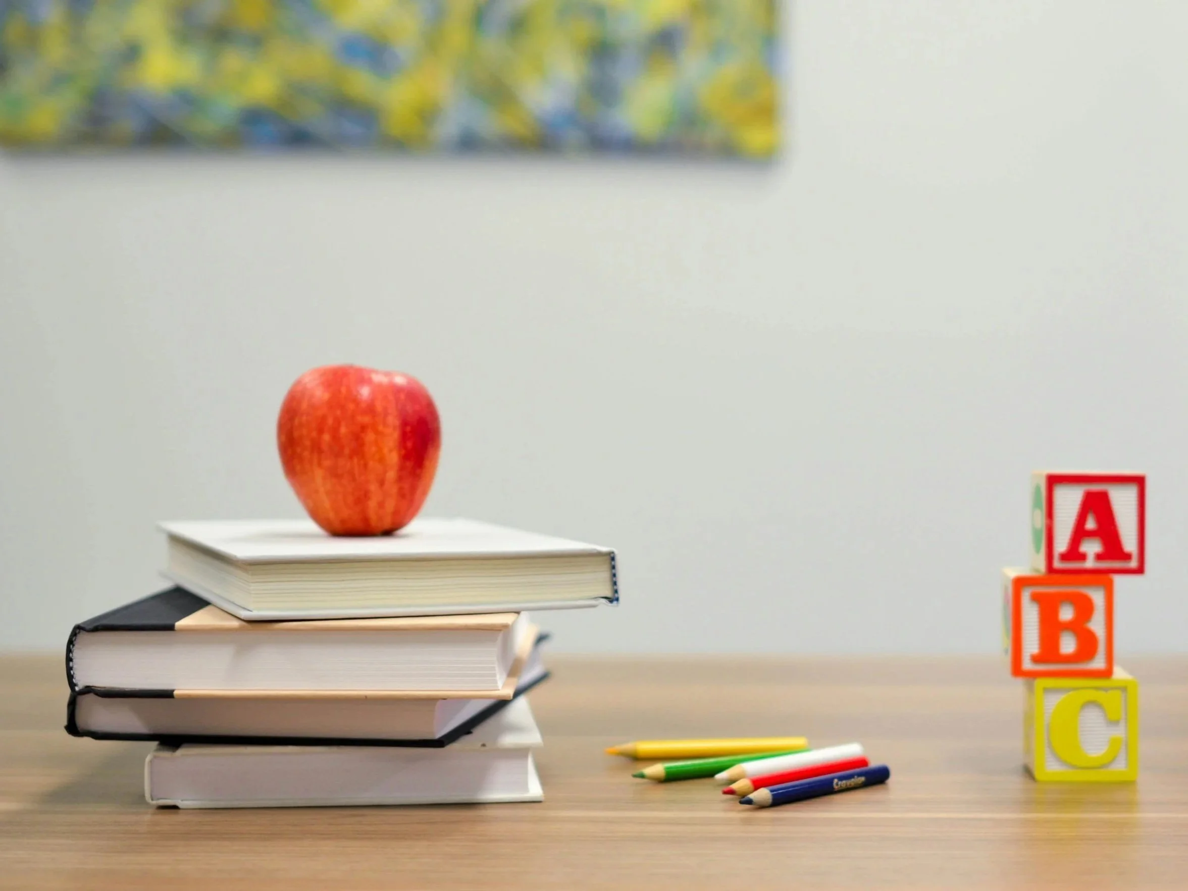 Stack of books with an apple on top, colored pencils, and ABC blocks on a wooden table.