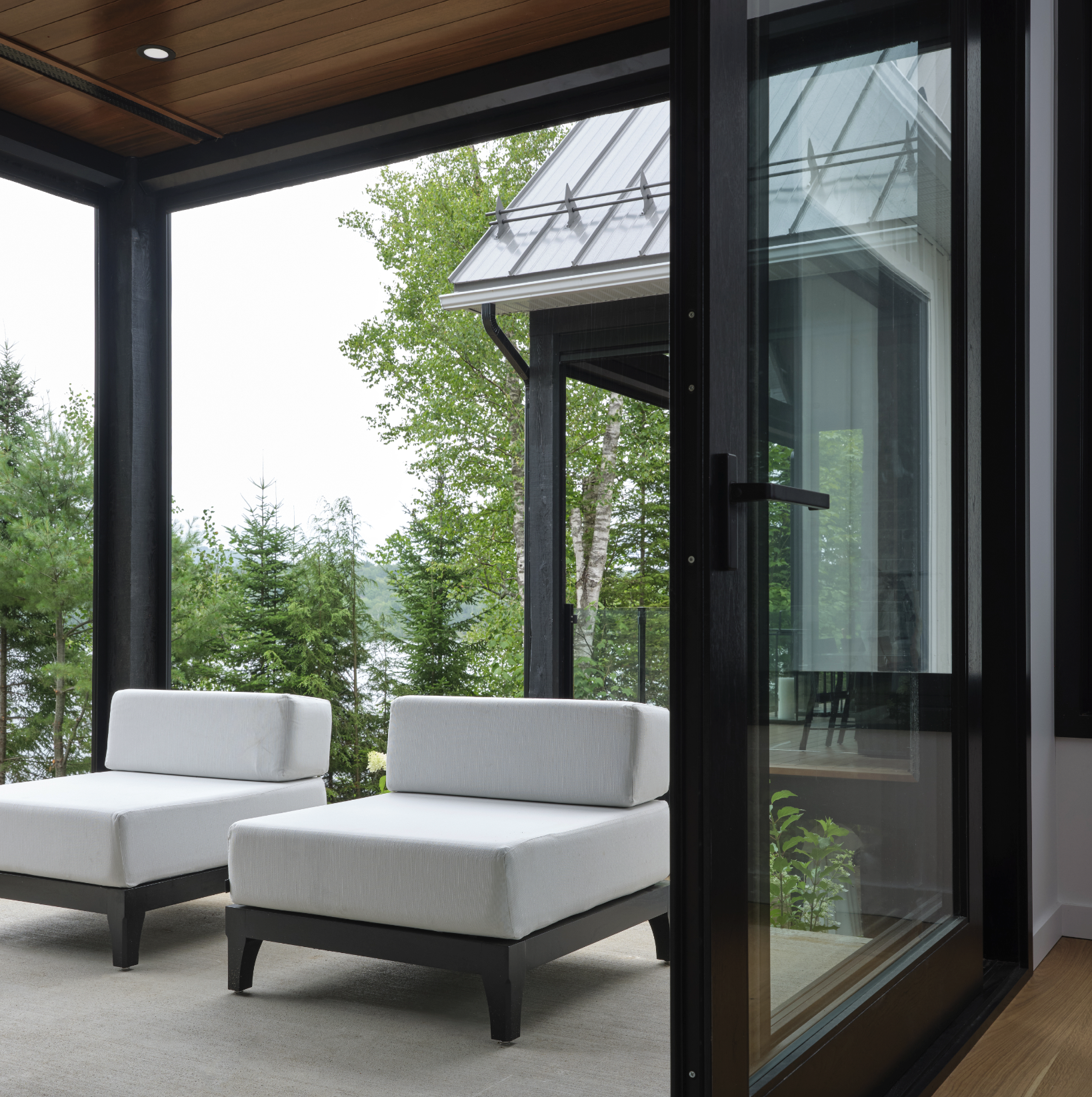 Deux fauteuils blancs sur une terrasse, entourés d'une structure en verre et d'arbres à l'arrière-plan.
