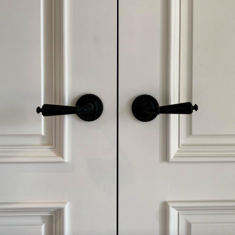 Deux poignées de porte noires sur des portes blanches à panneaux.