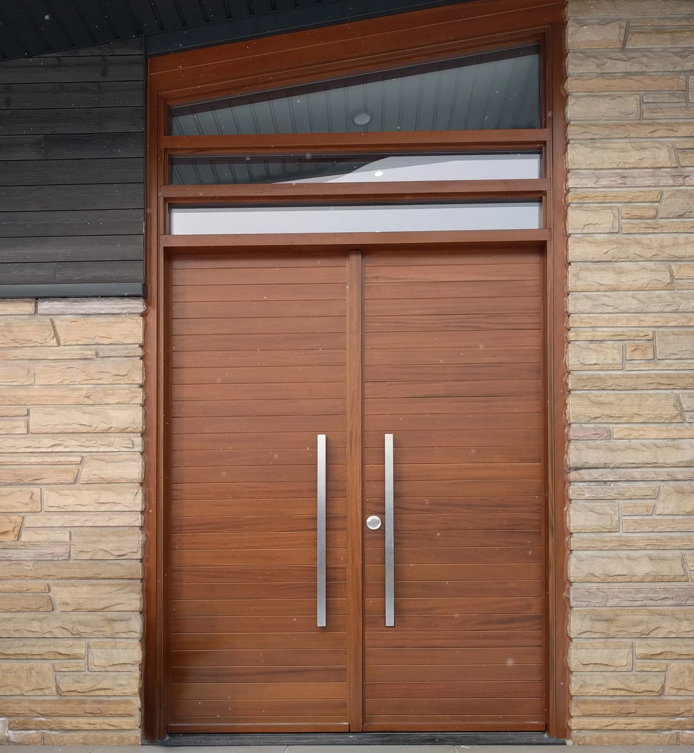 Porte en bois moderne avec poignée en métal, entourée de murs en pierre et bois sombre.