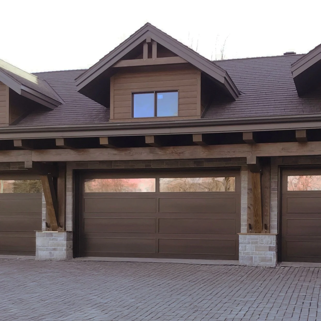 Porte de garage en bois massif brun clair avec fenêtrage, toiture en pente et revêtement extérieur en bois.