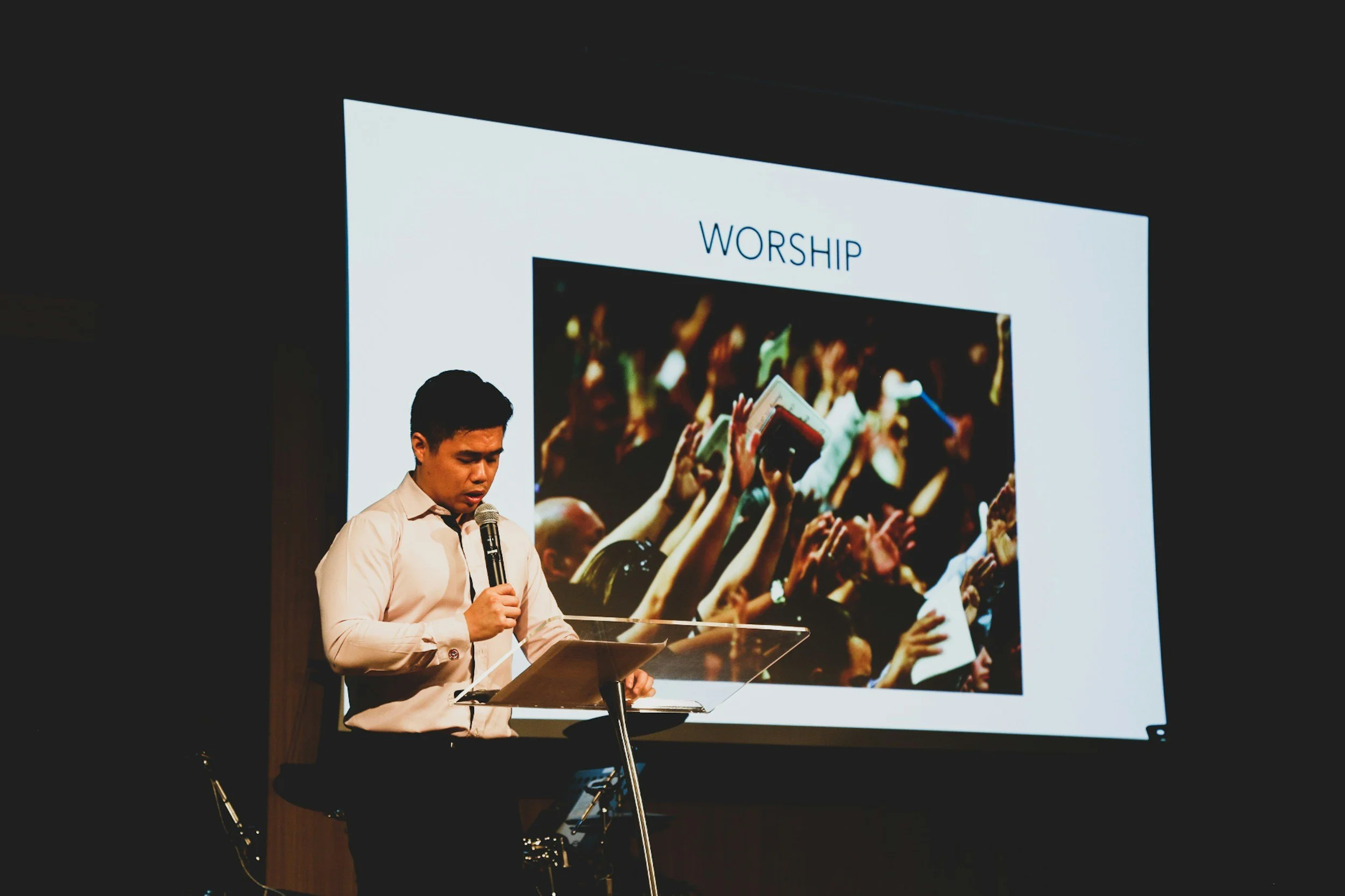 Speaker at podium with microphone in front of worship slide on screen