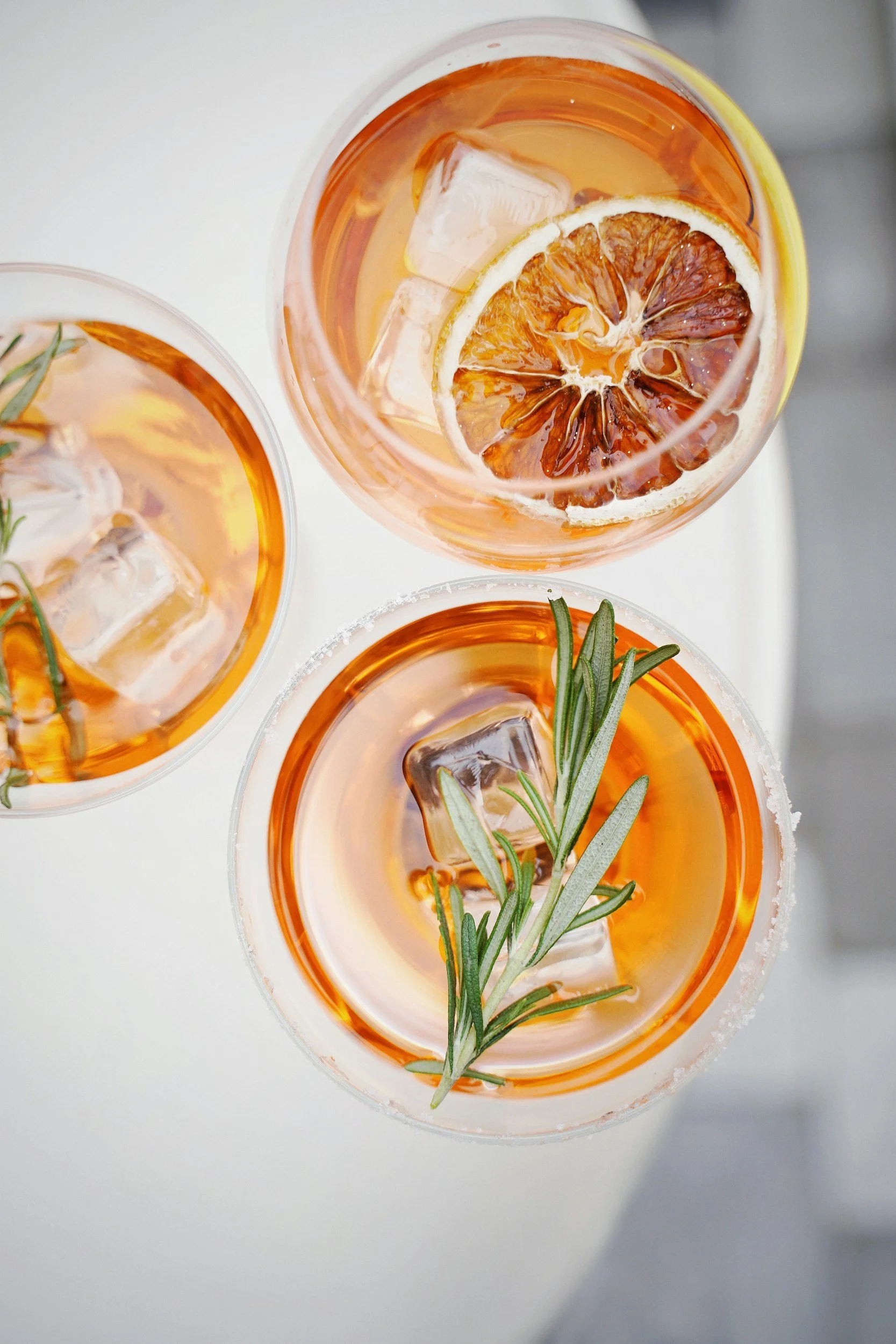 Three cocktail glasses  garnished with rosemary sprigs and lemon slices, viewed from above.