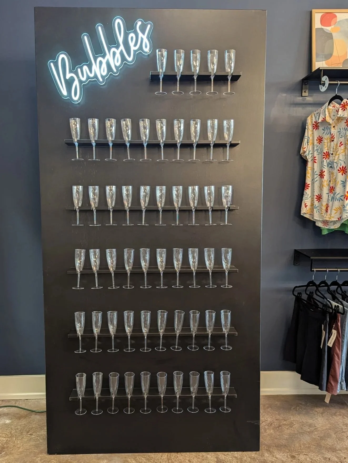 Large black wall with 55 champagne glasses, and a neon bubbles sign