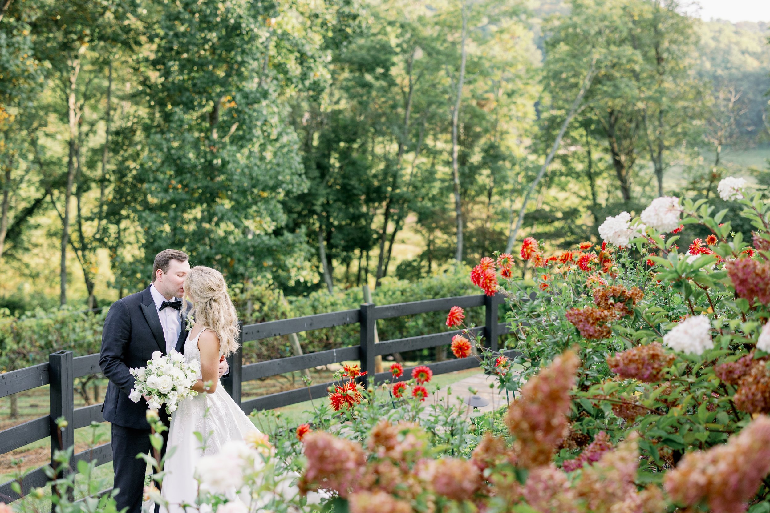 Bride and groom posing in front of vibrant summer blooms and mountain hydrangeas at a Highlands vineyard wedding.