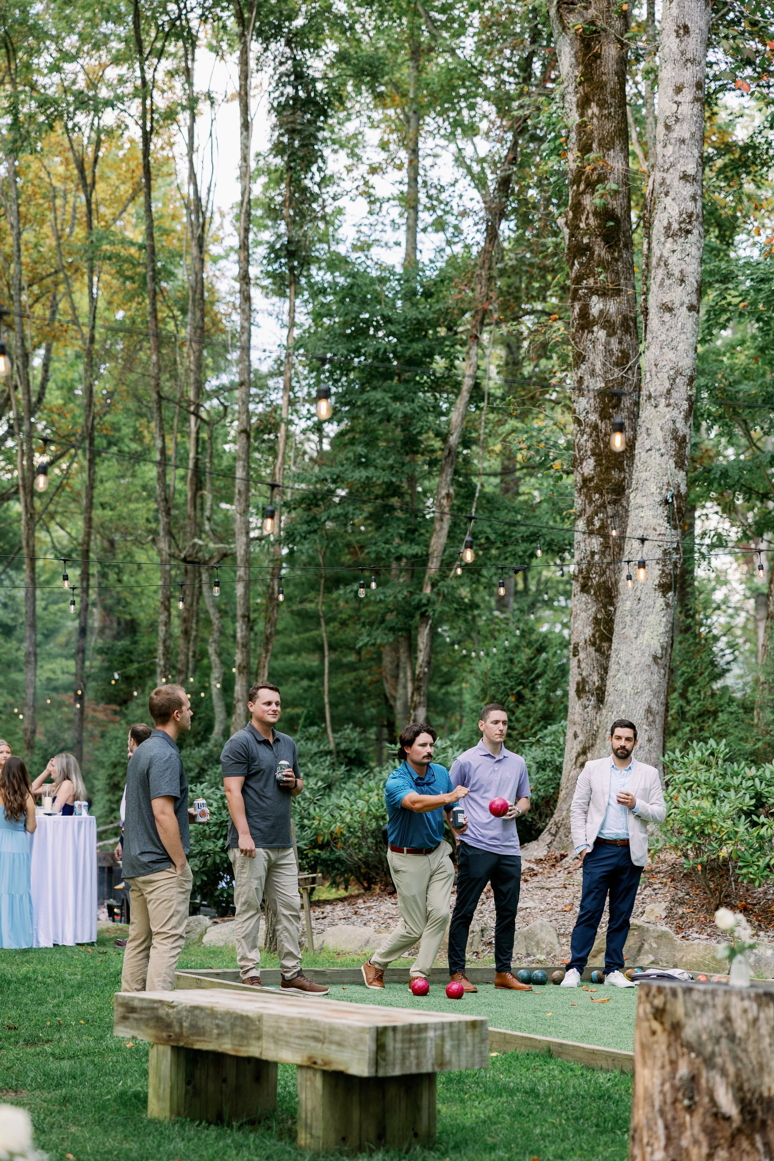 Men playing bocce ball on a manicured court surrounded by trees during a Labor Day weekend summer camp.