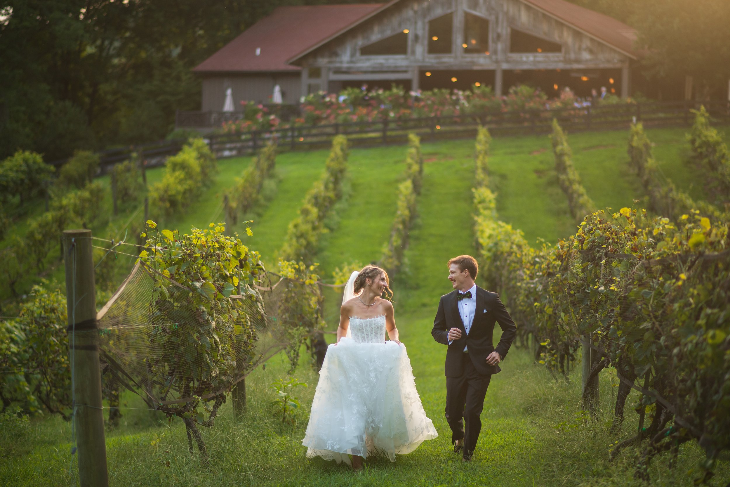 A newlywed couple frolicking through the grapevines at The Vineyard at High Holly, a premier mountain wedding venue in Highlands, NC.