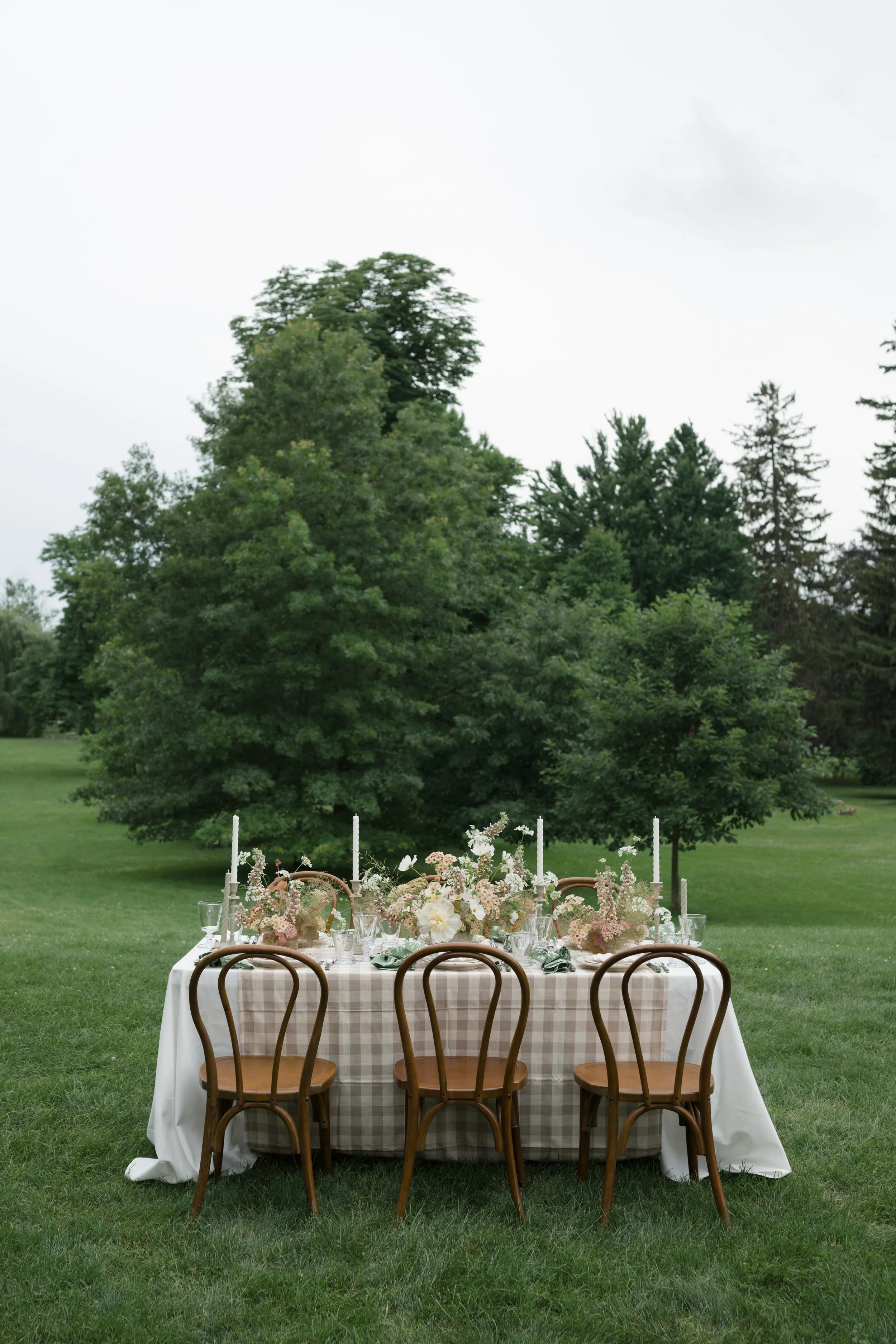 Sonnenberg Gardens, Canandaigua, NY Outdoor table set for a meal with floral centerpieces and candles, surrounded by four chairs, on a grassy lawn with trees in the background.