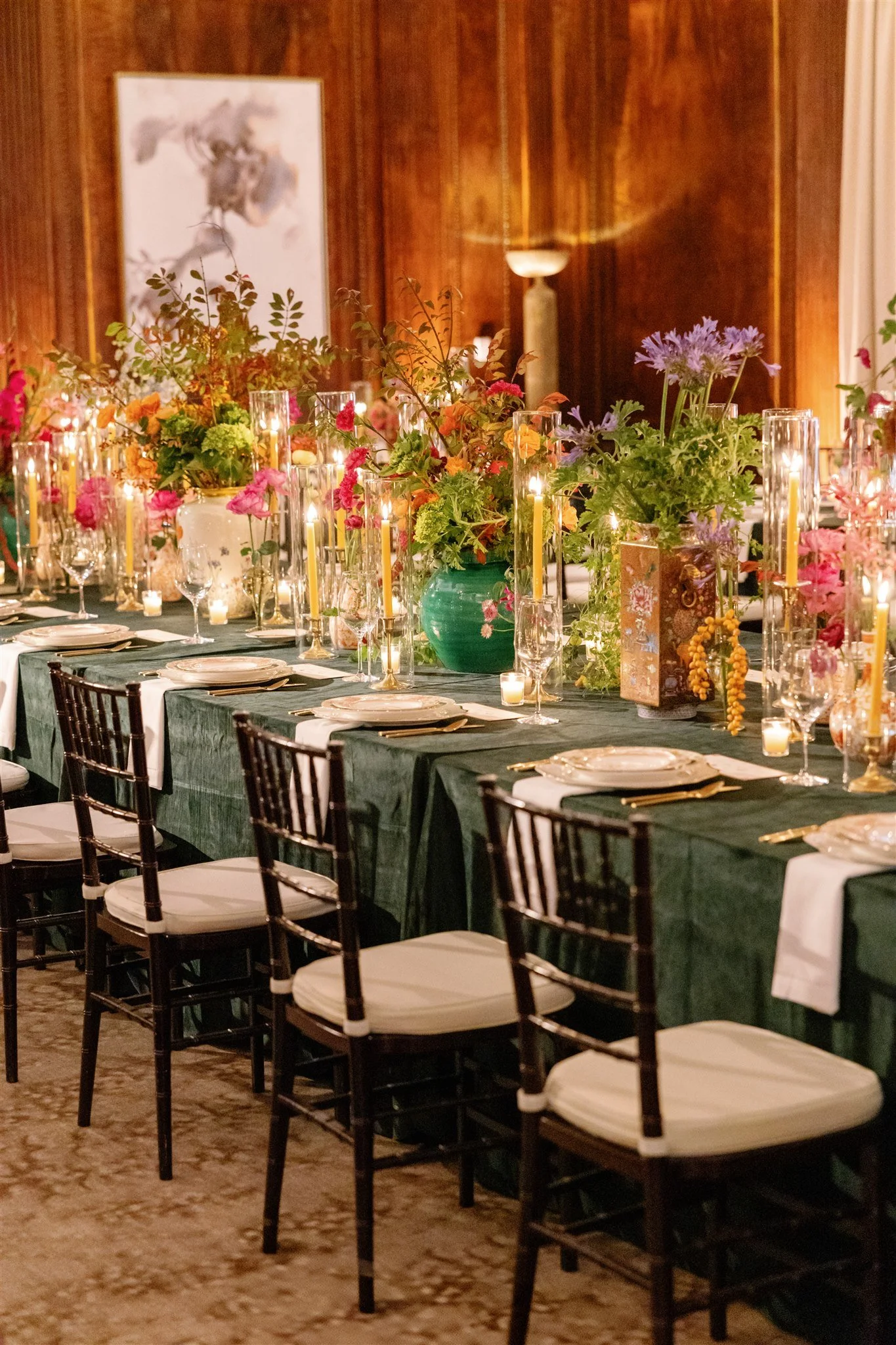 Elegant dining table with green tablecloth, floral centerpieces, and lit candles in a warmly lit room.