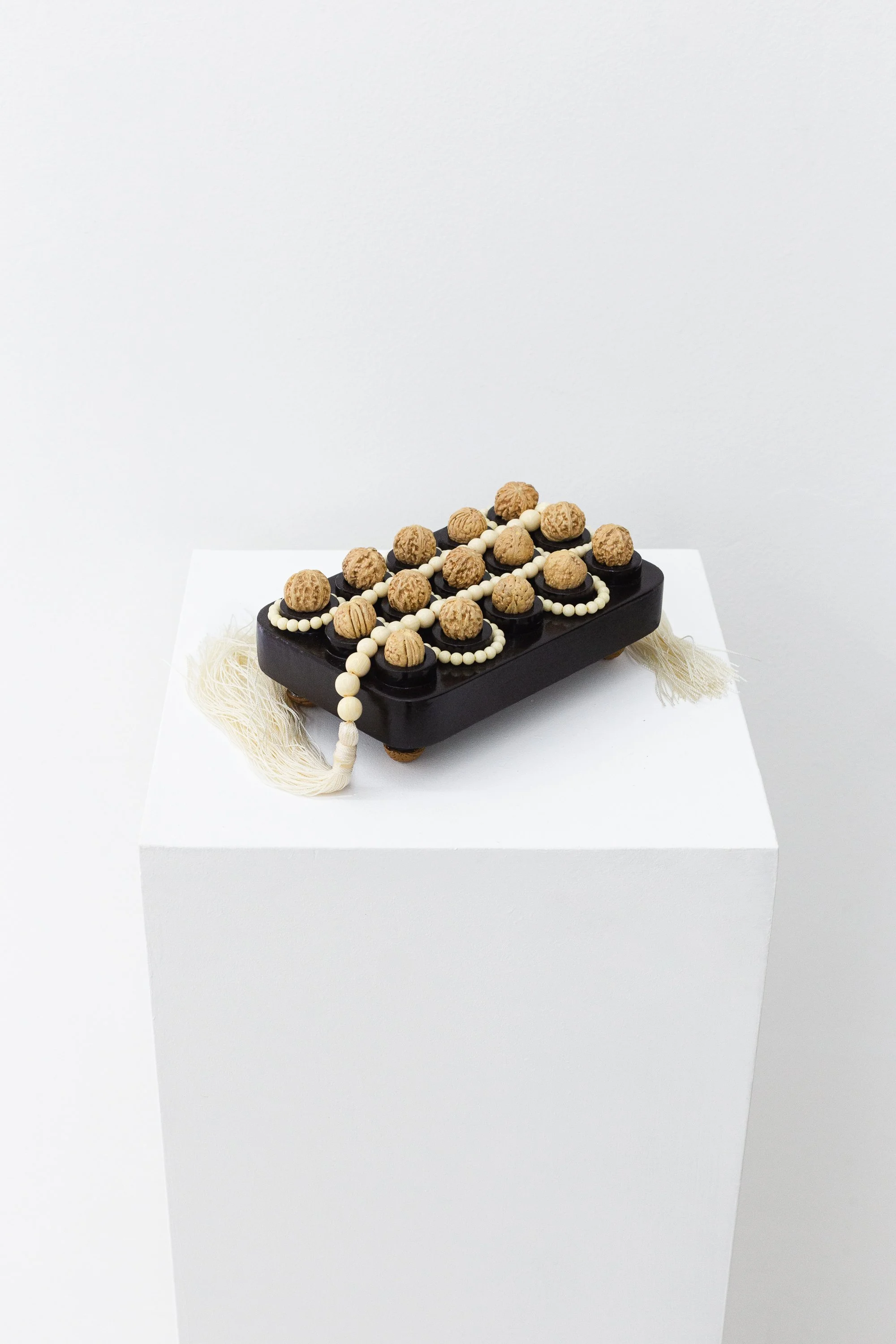 Sami E. Nicolle 
Juego del gusano blanco, 2026 
Resin beads, nuts, shellac, thread and painted MDF 
19 x 13 x 7.5 cm 
7.48 x 5.12 x 2.95 in. 