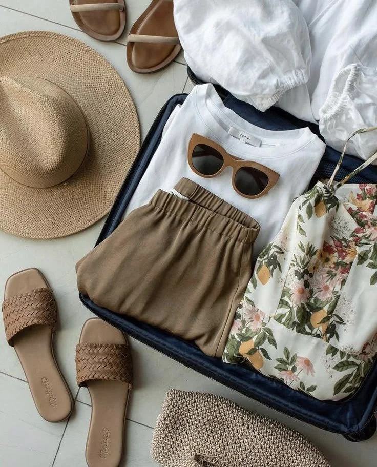 A straw hat with turquoise beads and a patterned blue and white scarf, along with sunglasses, hanging on a white wooden wall.