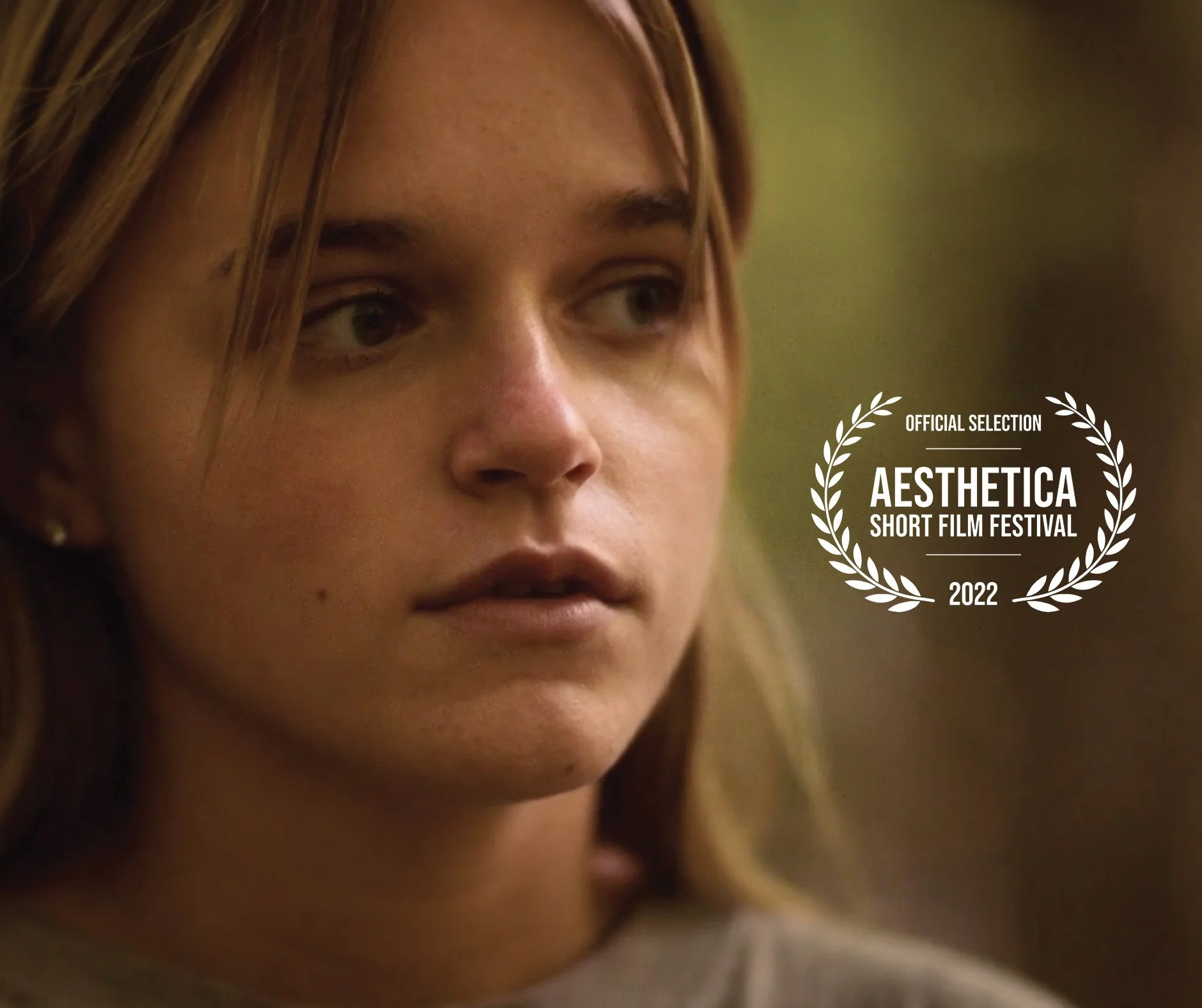 Portrait d'une femme avec expression sérieuse, texte indiquant "OFFICIAL SELECTION AESTHETICA SHORT FILM FESTIVAL 2022" à droite de l'image.