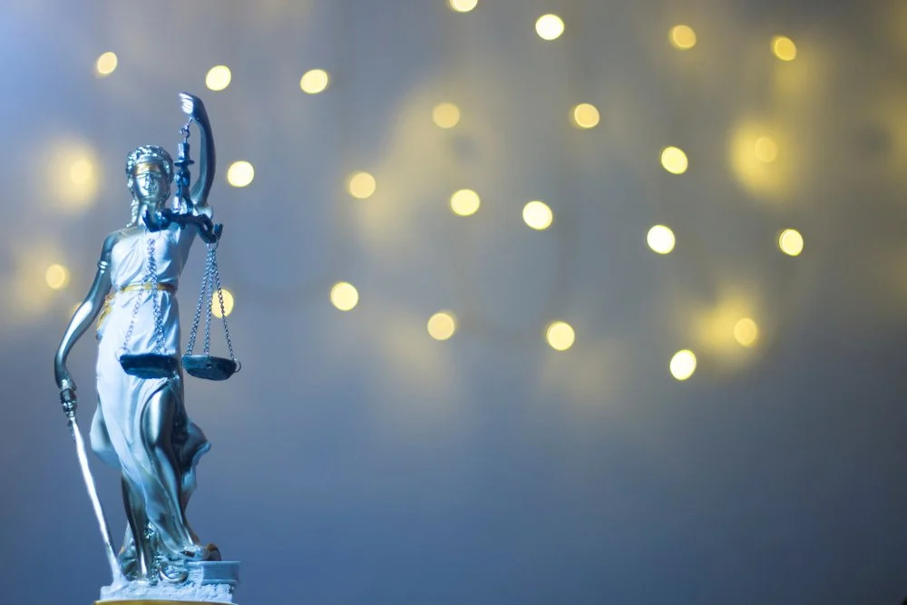Statue of Lady Justice with scales, sword, and blindfold, against a background of blurred lights.