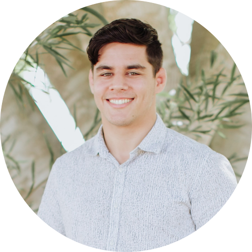 Luke Warren, Youth Group Team Leader, A young man with dark hair, smiling, wearing a light gray patterned button-up shirt, standing outdoors in front of greenery and tree trunks.