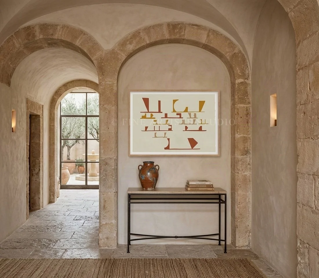 Horizontal abstract fine art print in a natural wood frame hanging over a black wrought-iron console table inside a luxury stone villa with sweeping sandstone arches.