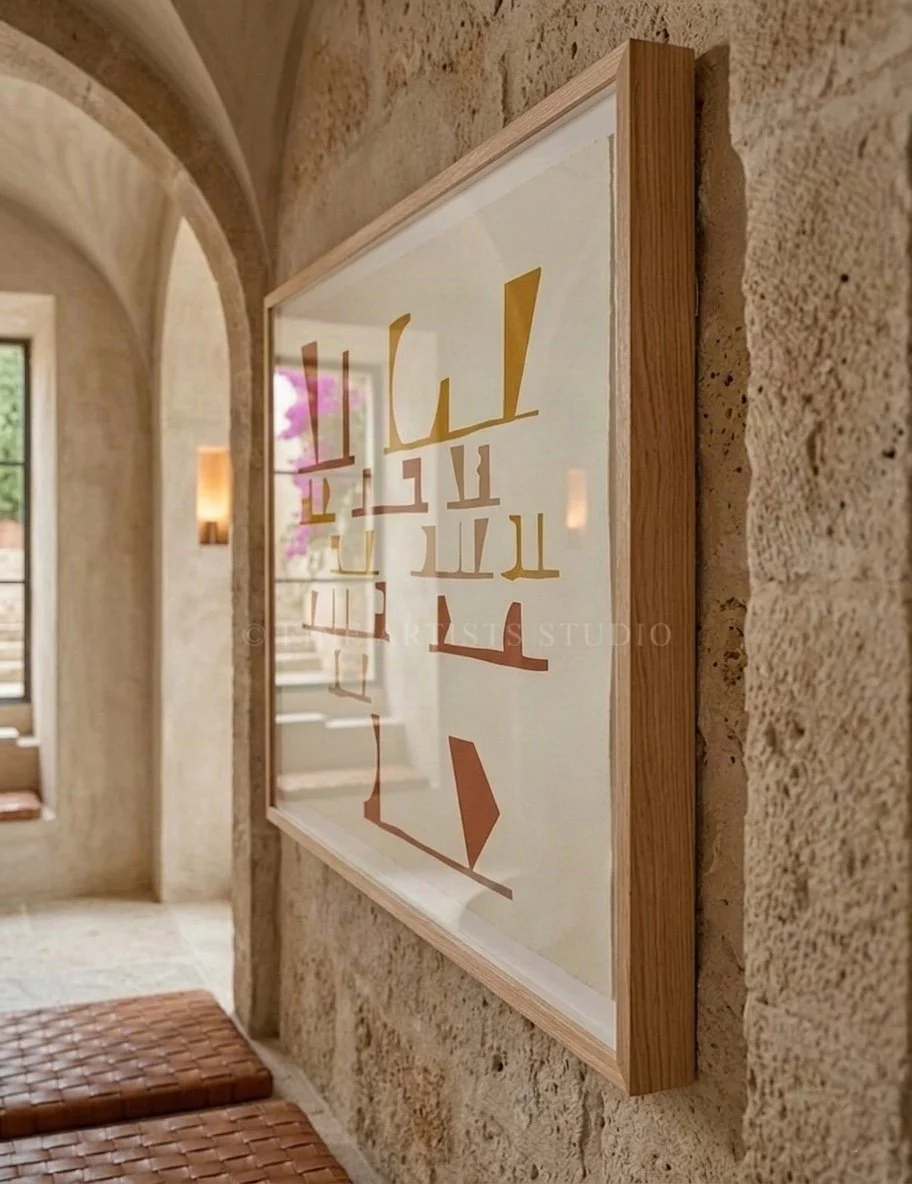 Angled close-up of a framed abstract print mounted on a textured, rustic limestone wall inside a Mediterranean home with warm lighting and leather benches.