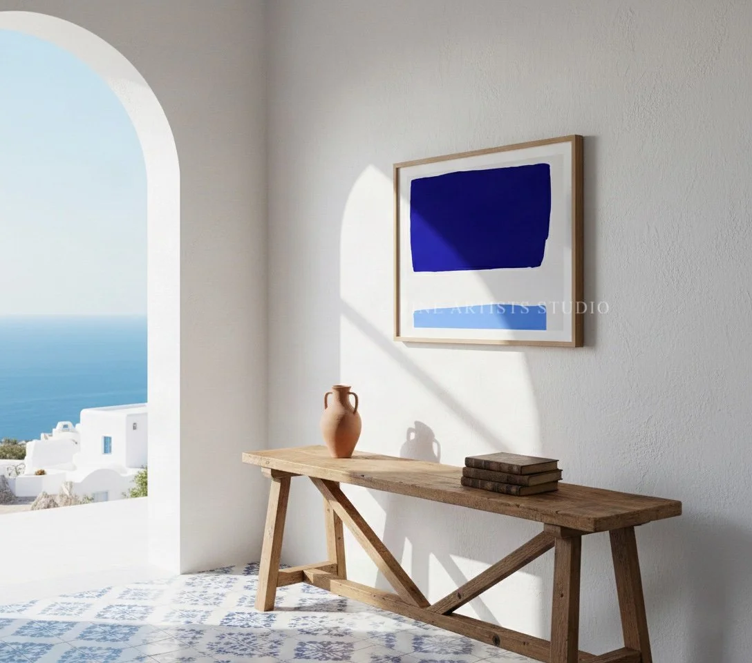 Framed cobalt and sky blue modern geometric print displayed on a wooden sideboard cabinet next to a sleek table and minimalist ceramics.