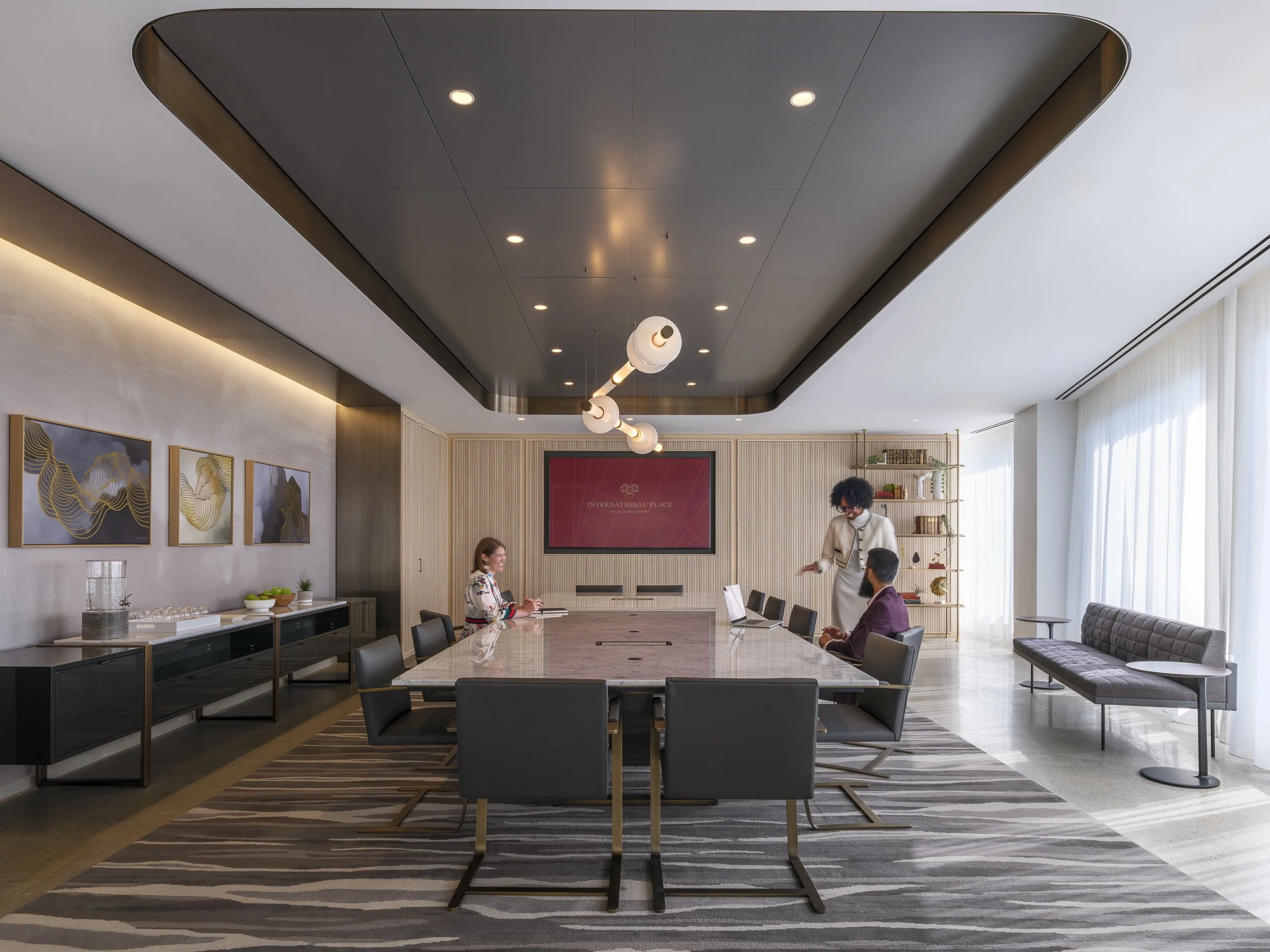 Big high end conference room with three people all dressed well 