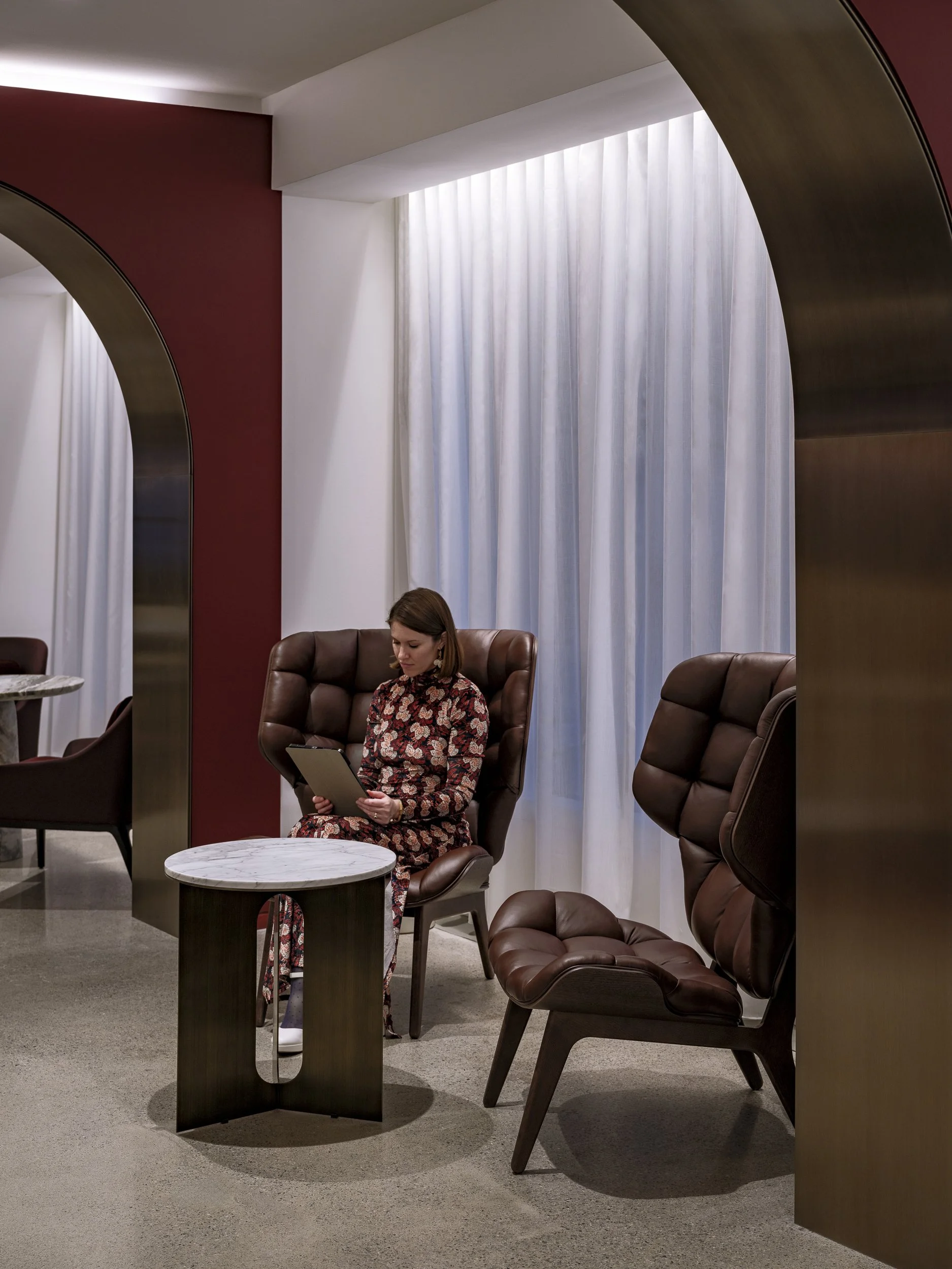 Main Lobby Aries Club Designed by Gensler woman sitting in modern maroon high back chair 