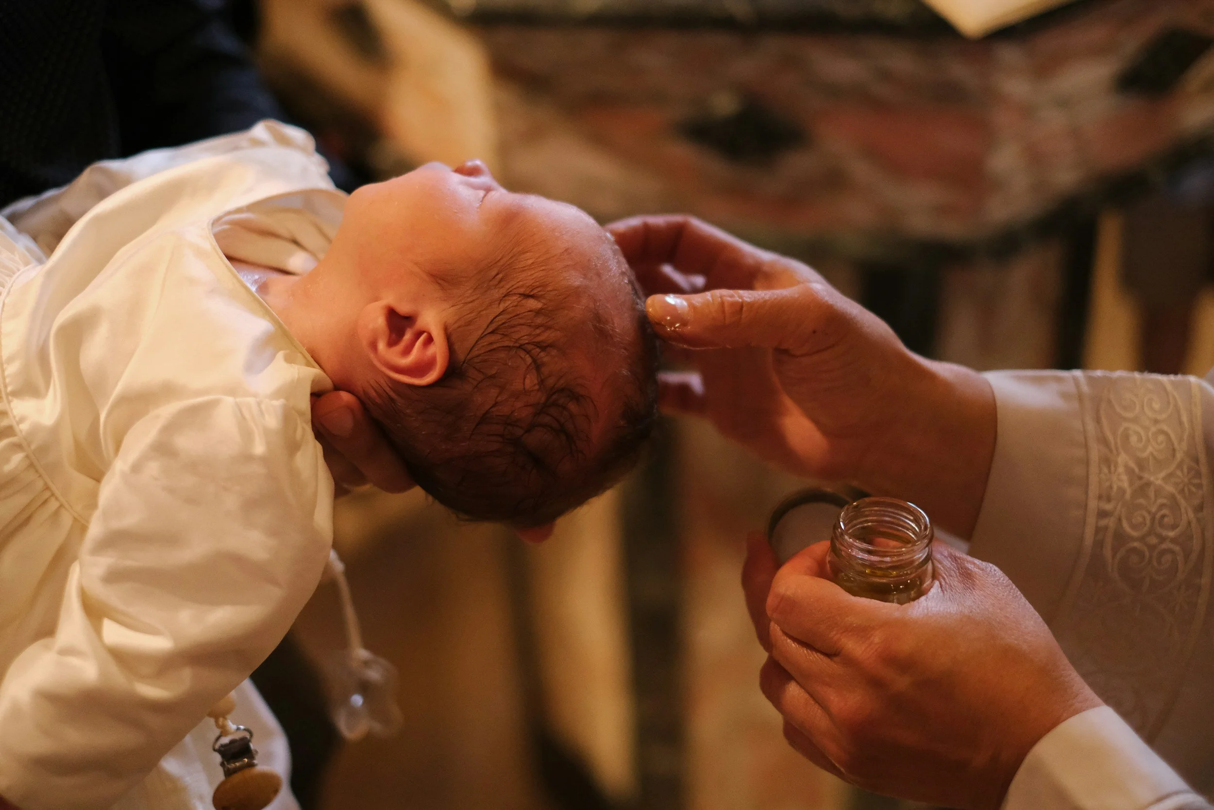 Un bebé siendo ungido con aceite por un sacerdote durante un sacramento religioso.