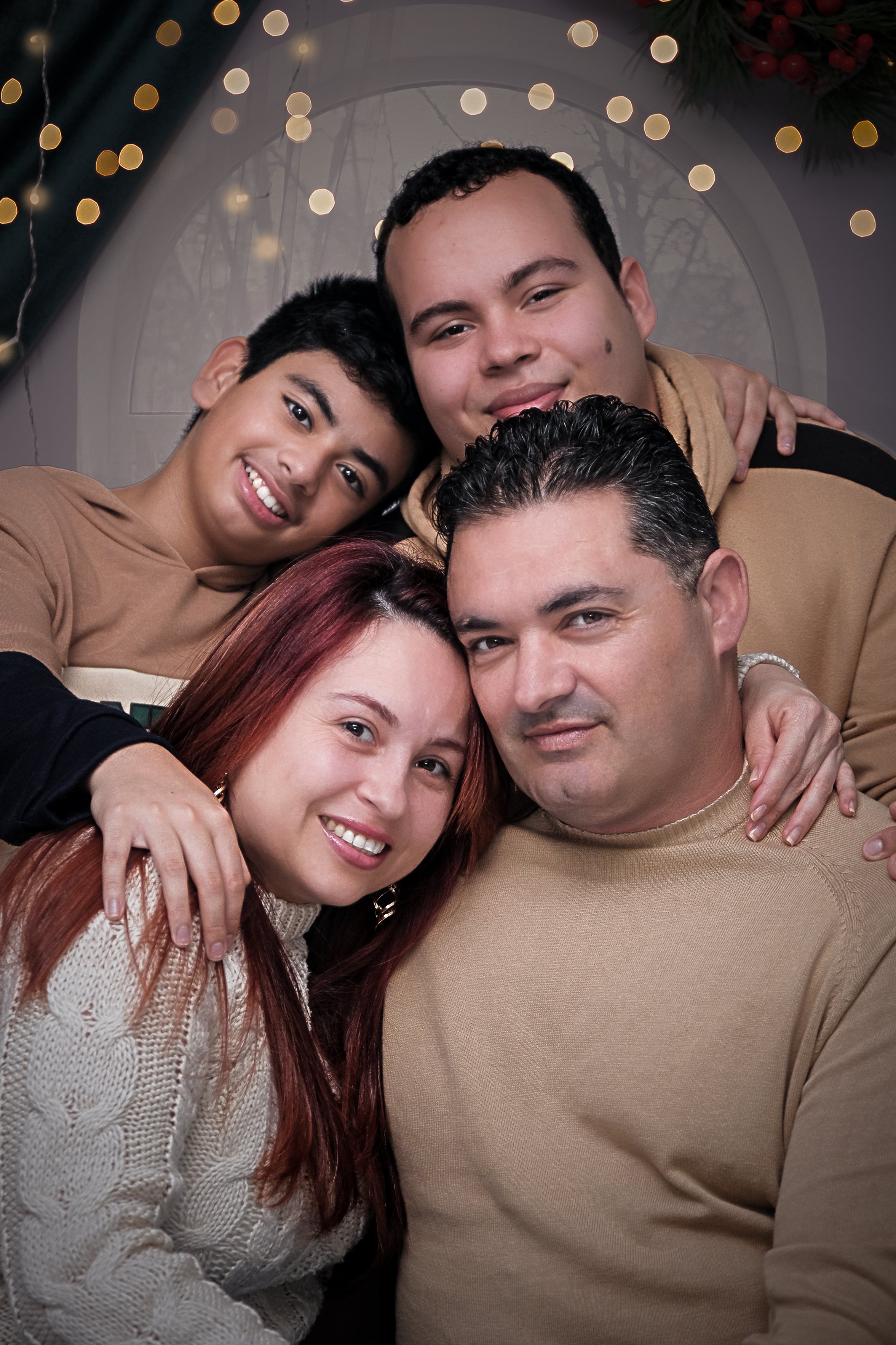 Un grupo de cinco personas, adultos jóvenes y adultos, posando juntas en un ambiente festivo con decoraciones de Navidad, luces y una ventana en el fondo.