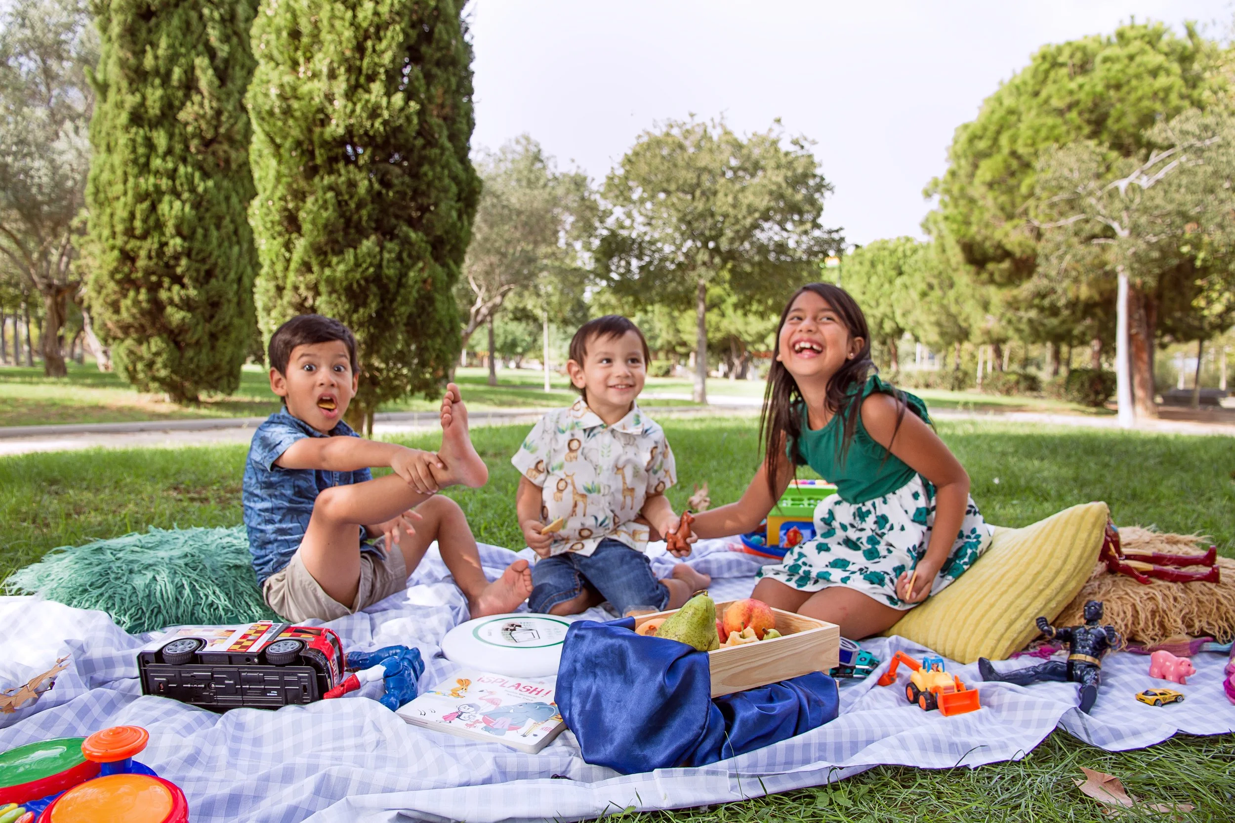 Niños jugando y sonriendo en un picnic en un parque con árboles y césped.