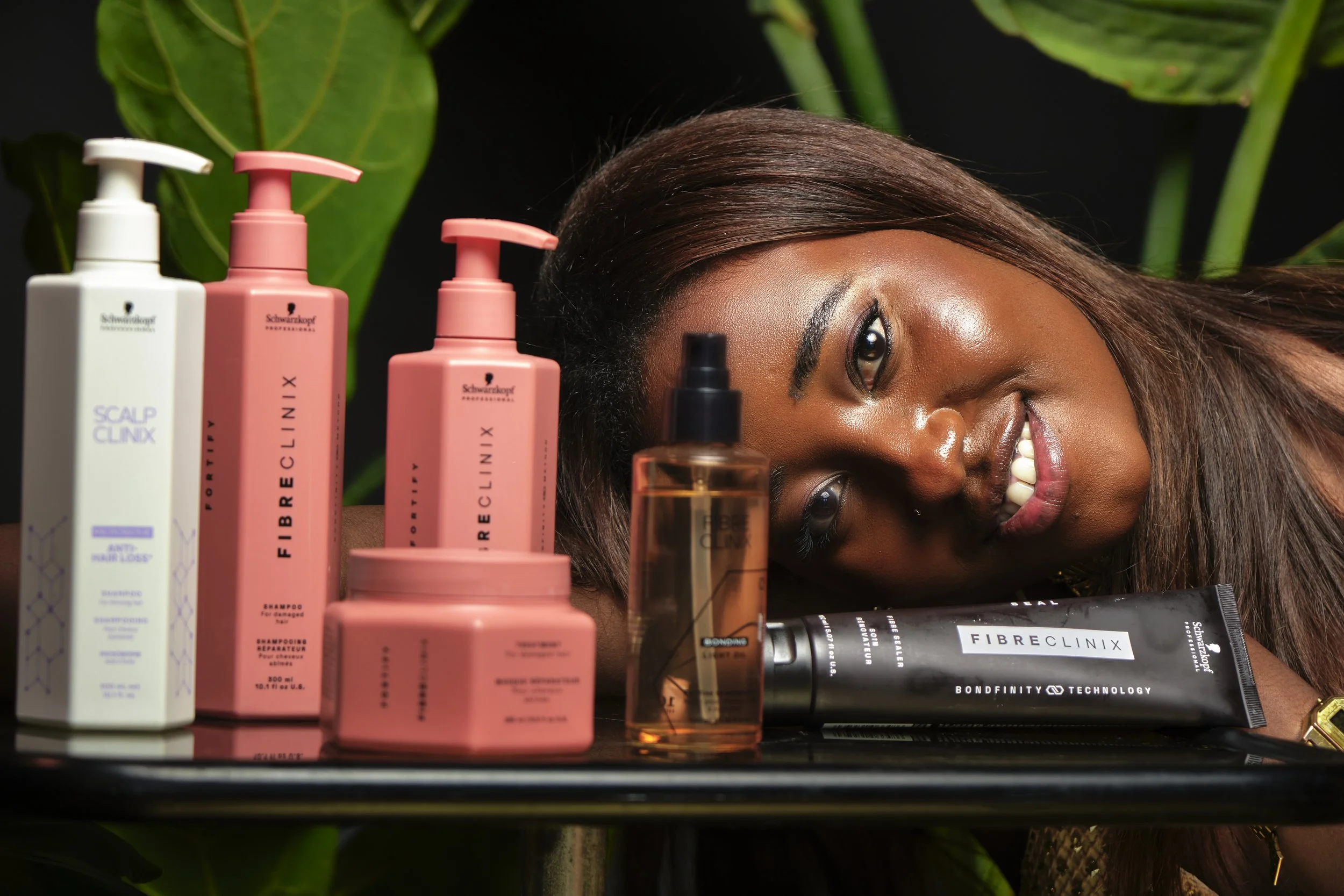 Mujer acostada entre productos para el cuidado del cabello en un fondo de hojas verdes.