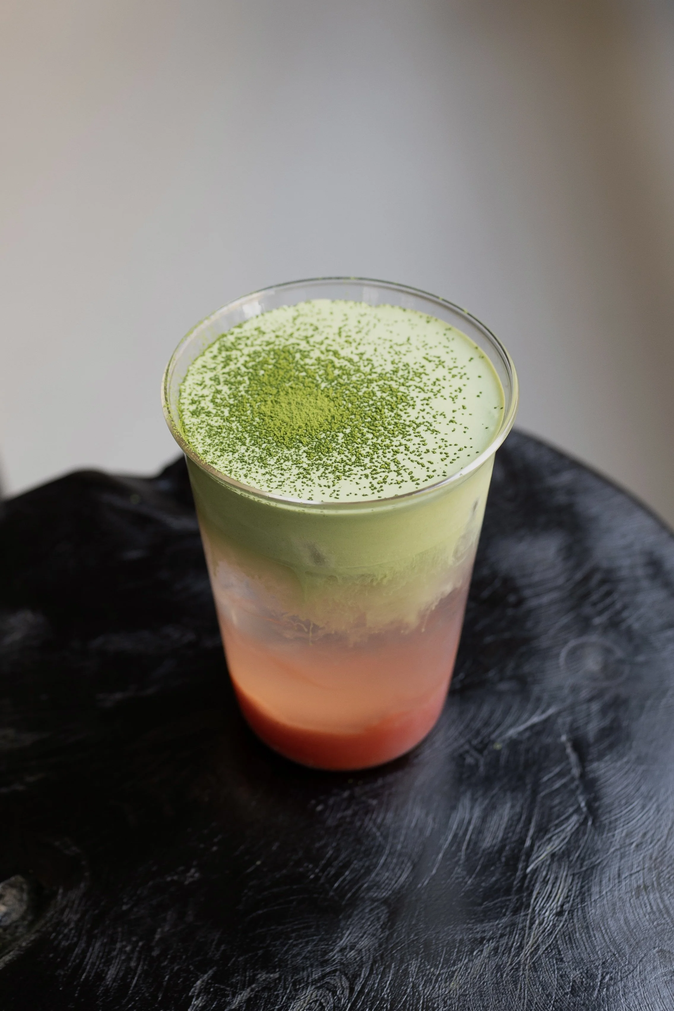 Un bicchiere con un drink colorato sfumato dal rosa in basso al verde chiaro in alto, con superficie verde di polvere di matcha