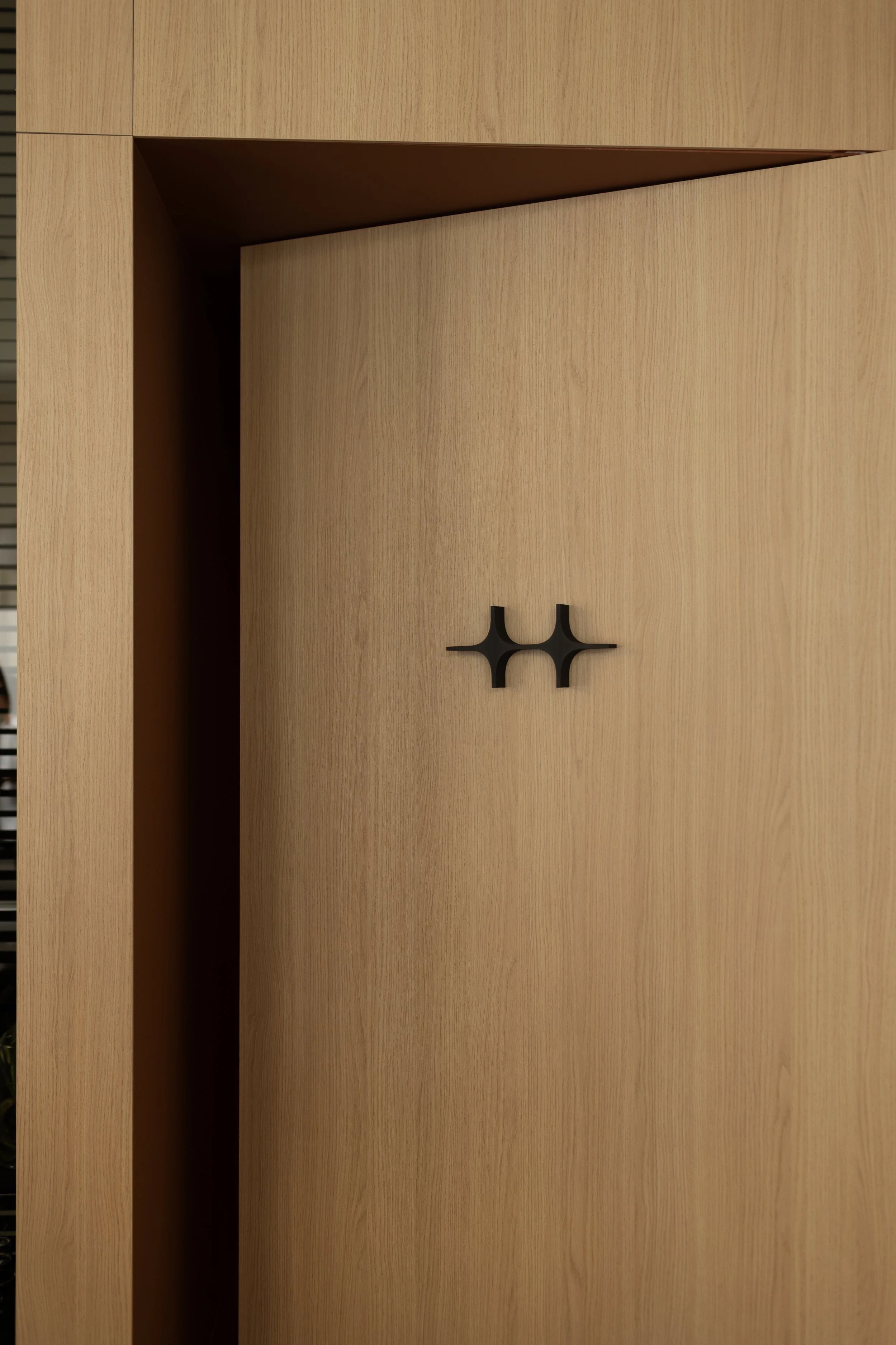 Porta di un armadio in legno chiaro con maniglia nera a forma di doppia croce.