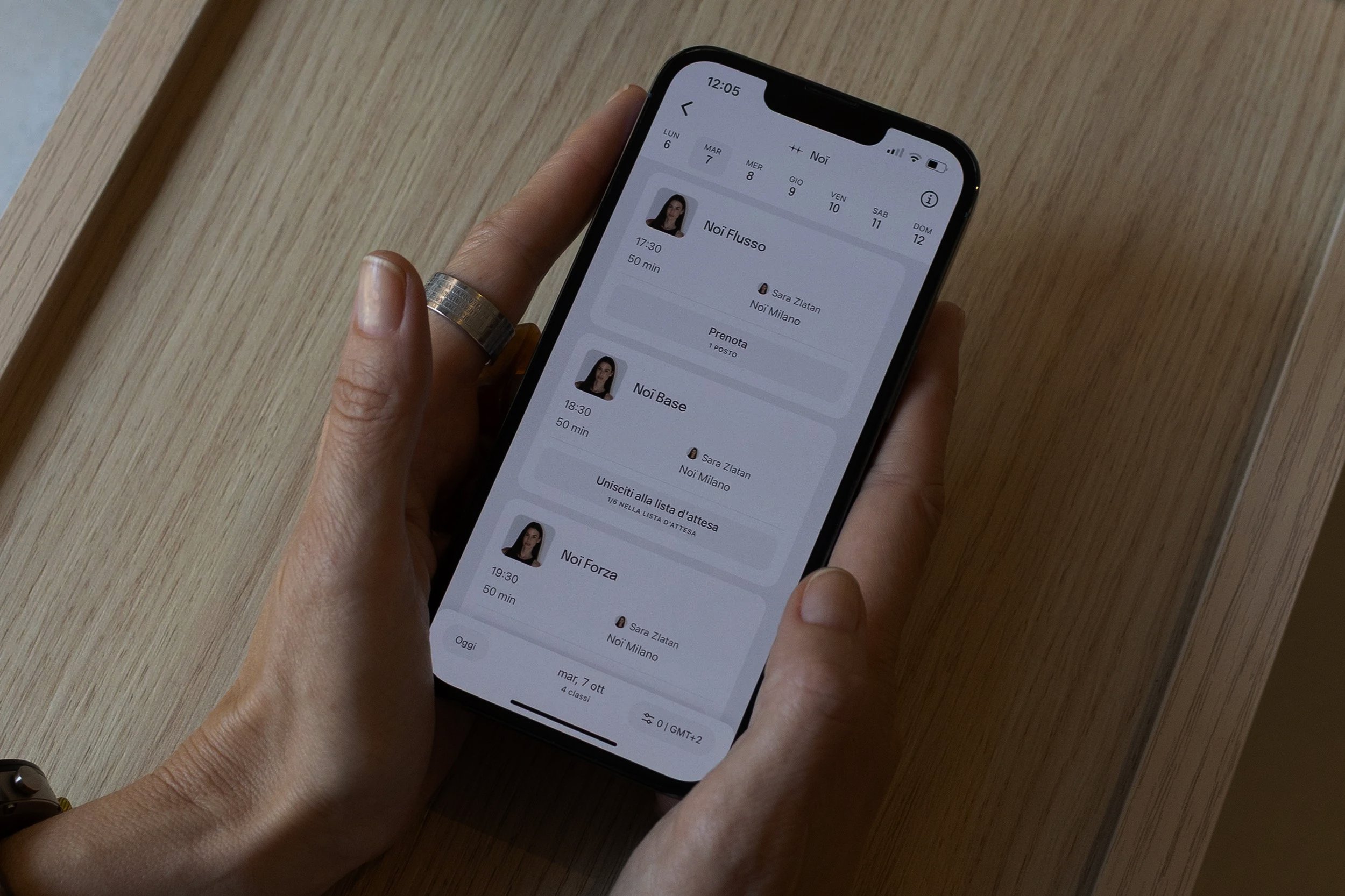 Una mano che tiene uno smartphone. Lo schermo dello smartphone mostra un'app di pianificazione o calendario con appuntamenti e profili di contatti.