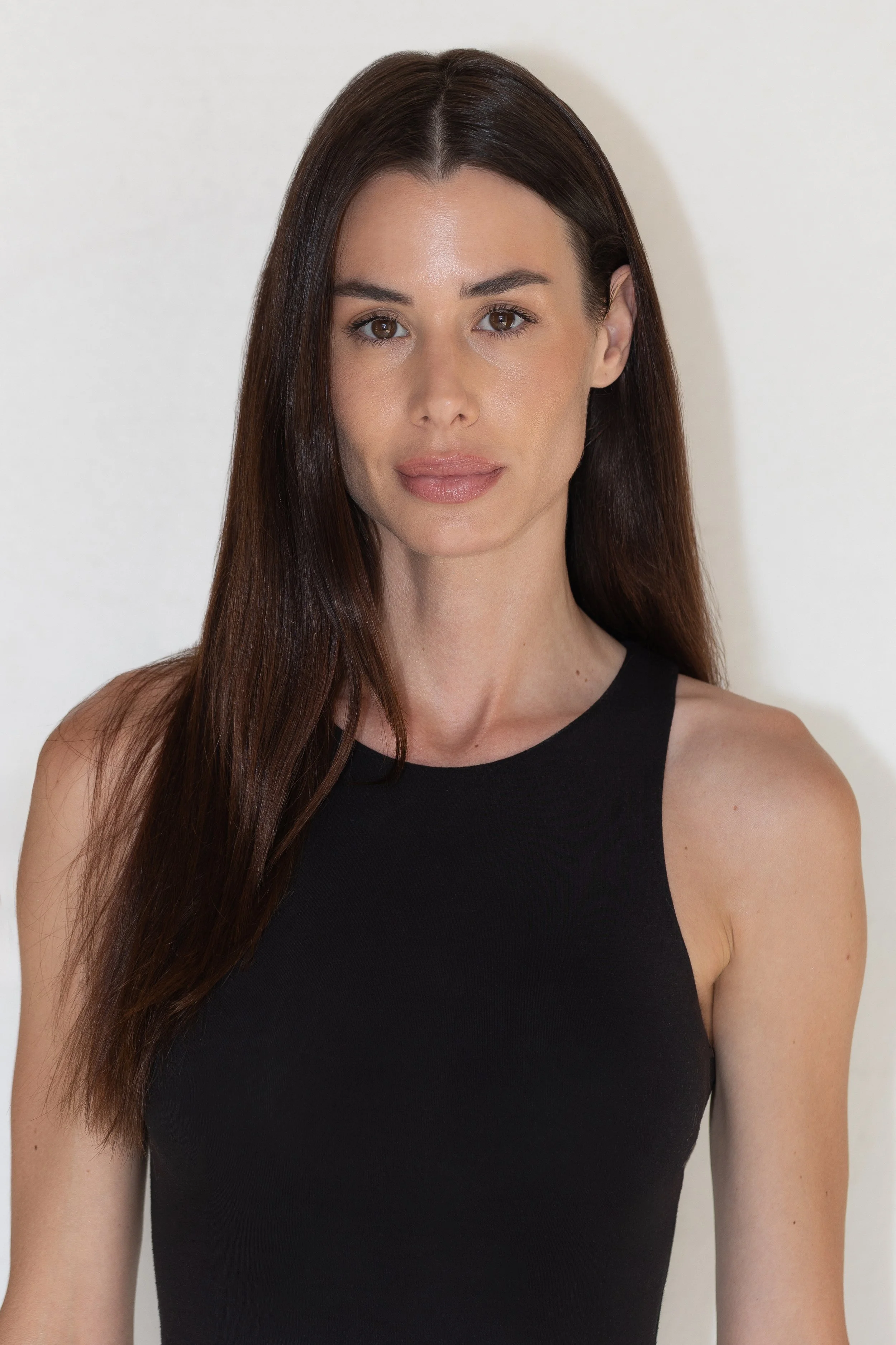 Ritratto di una donna con capelli lunghi e castani, indossa un top nero, sfondo bianco.