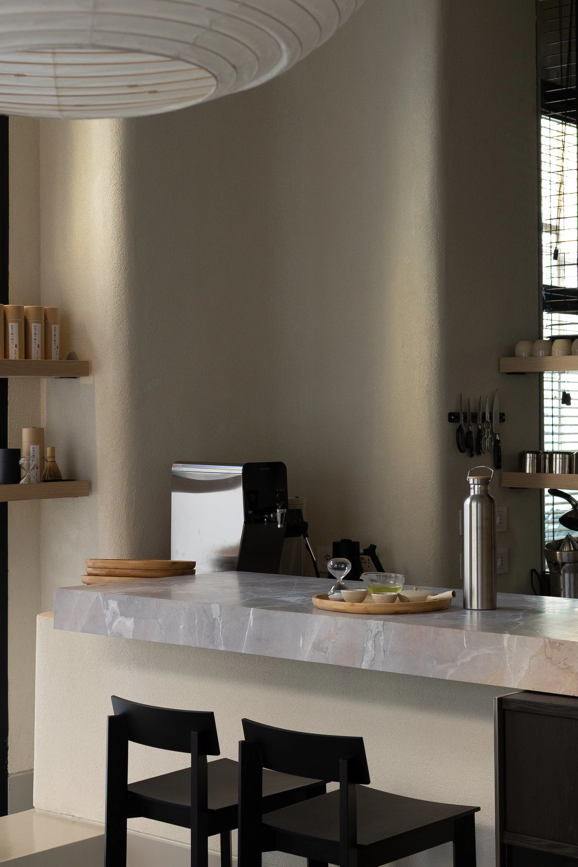 Interno di una cucina moderna con piano di lavoro in marmo, stoviglie, penne, attrezzature da cucina e sedie nere.