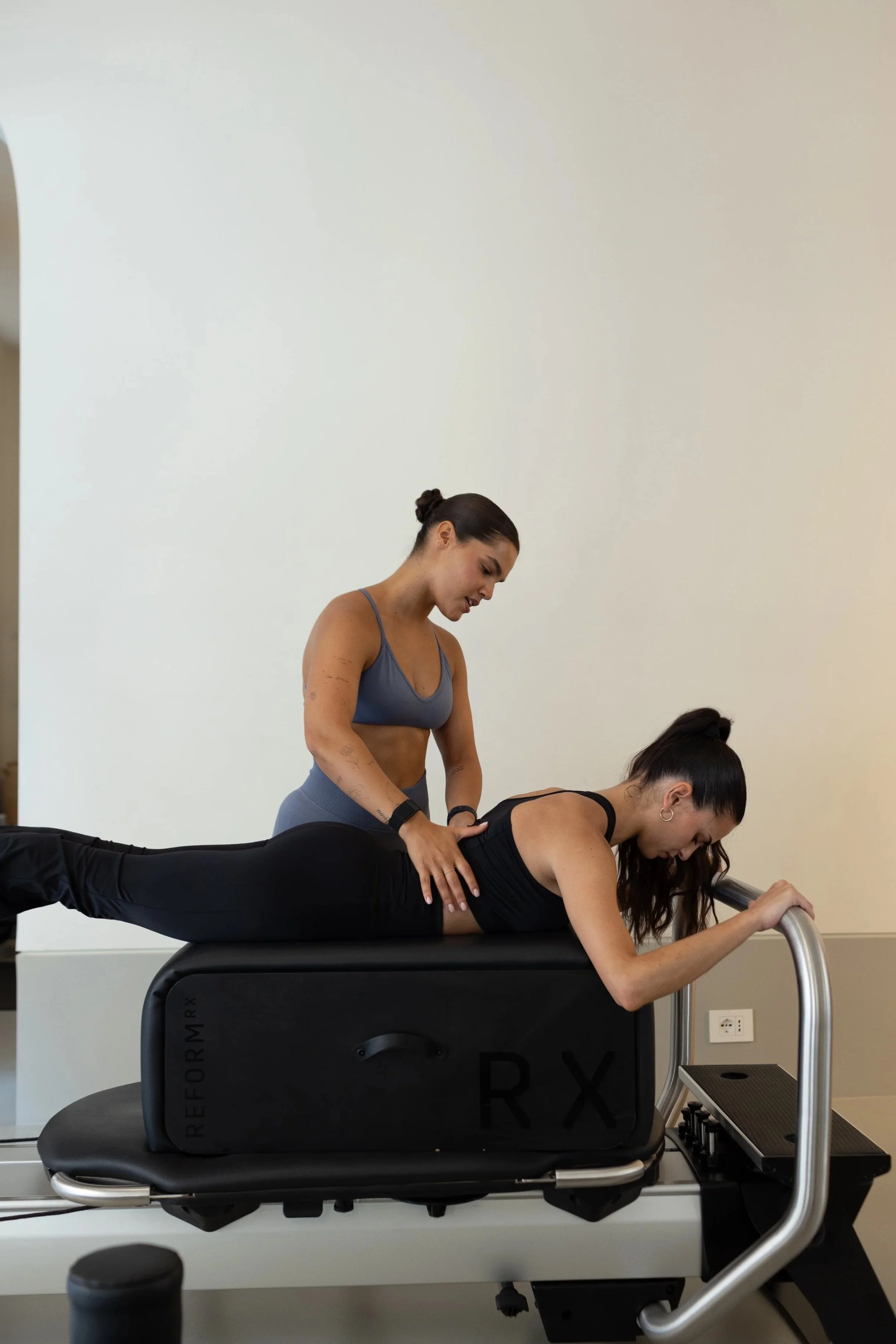 Una donna esegue un esercizio di plank su un'apparecchiatura di riabilitazione, mentre un'altra donna la supporta, in un ambiente di fisioterapia o pilates.